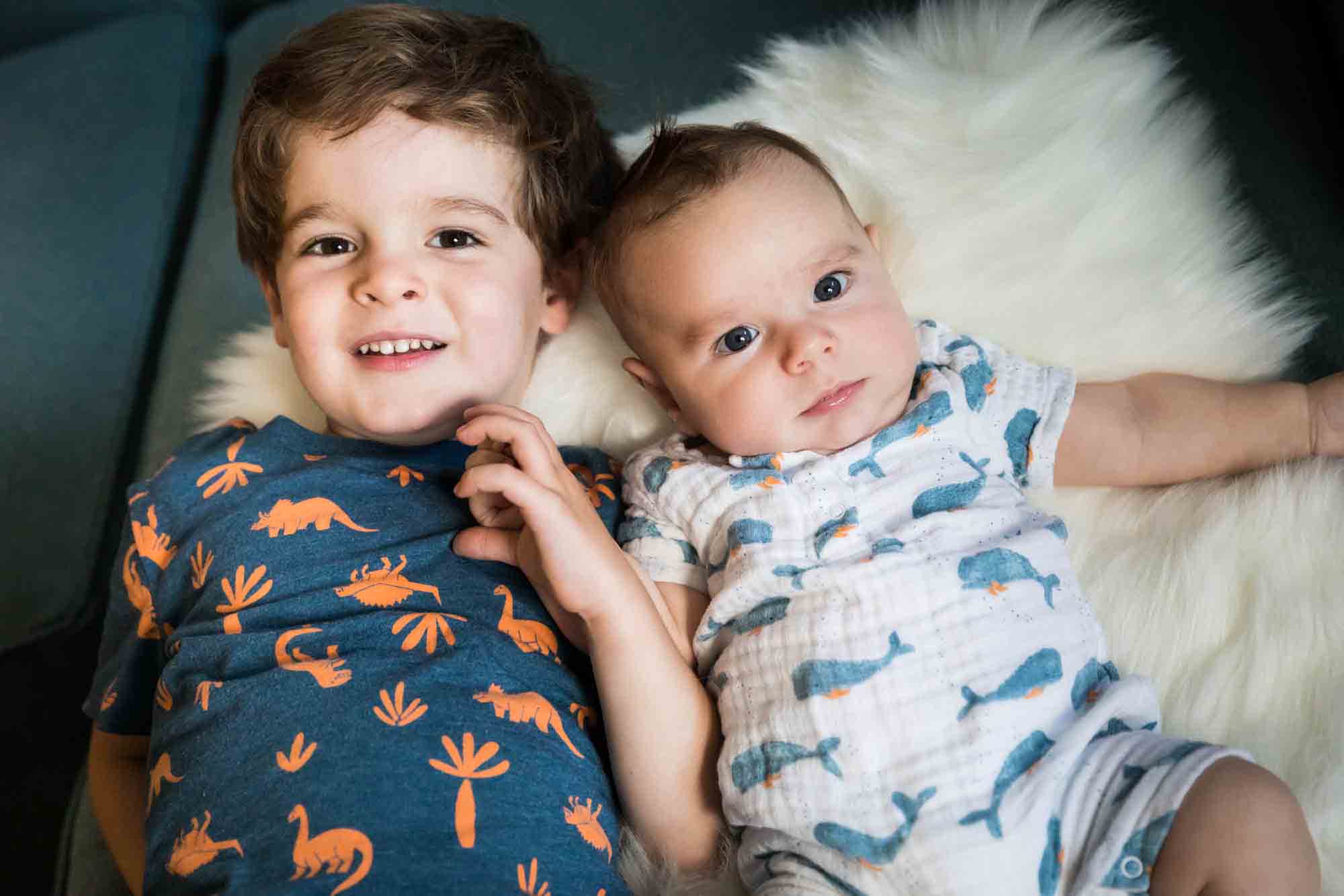 Little boy and his newborn brother lying on white rug