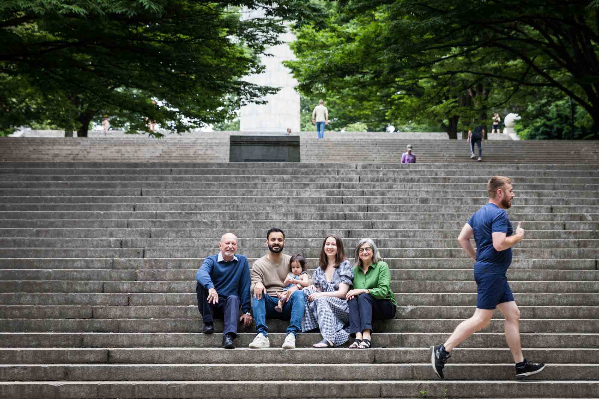 Family sitting on stone steps as jogger runs past