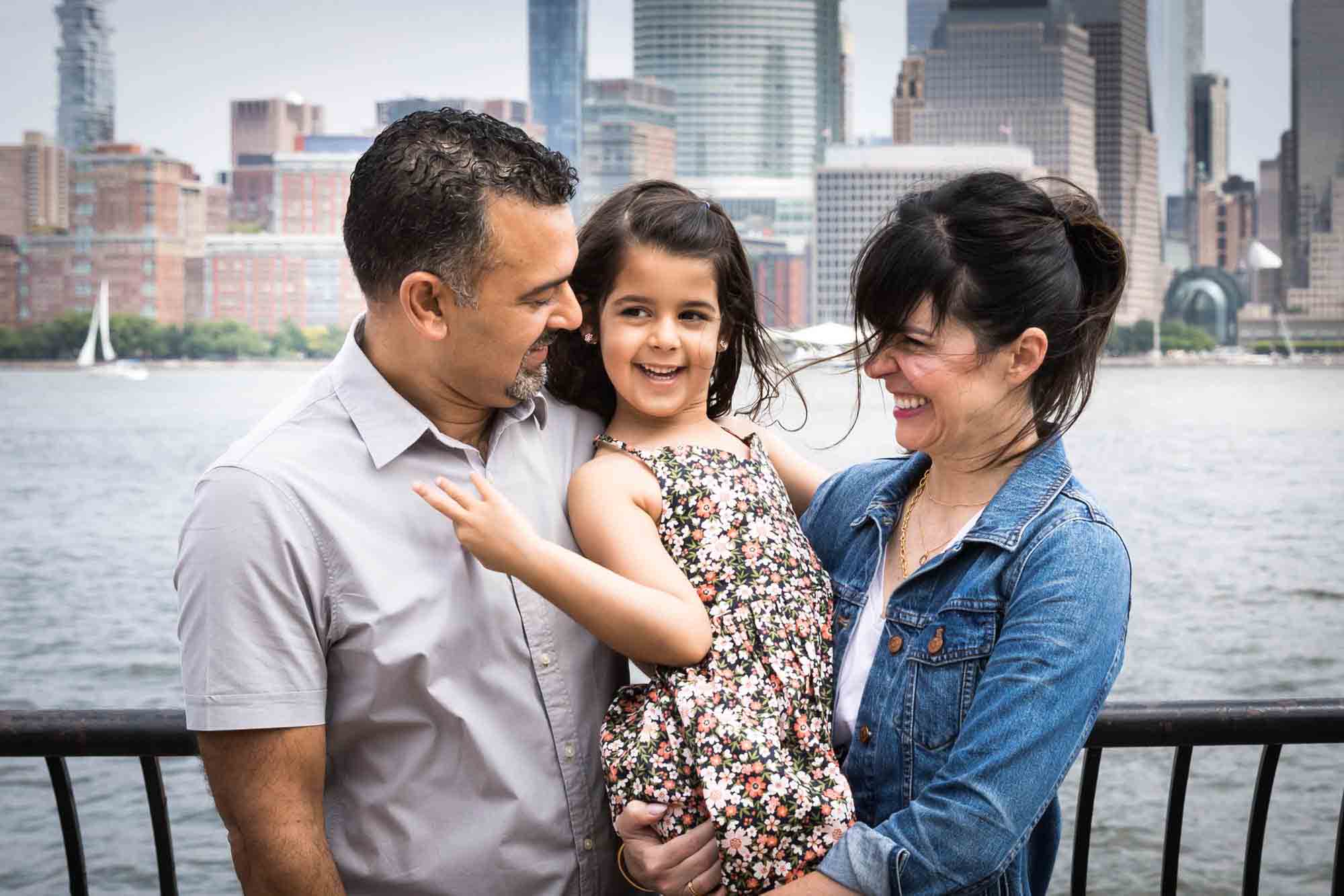 Little girl smiling while being held by parents in front of NYC skyline