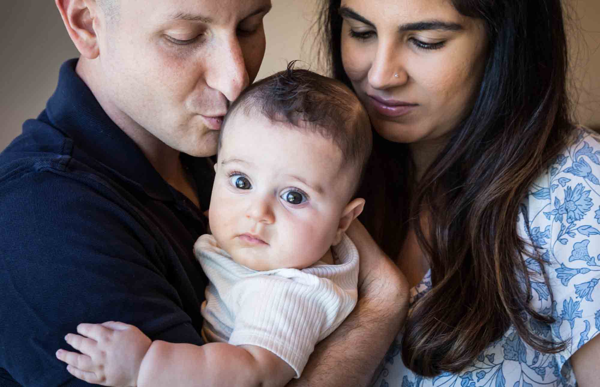 Parents kissing head of newborn son for an article advertising family portrait gift certificates