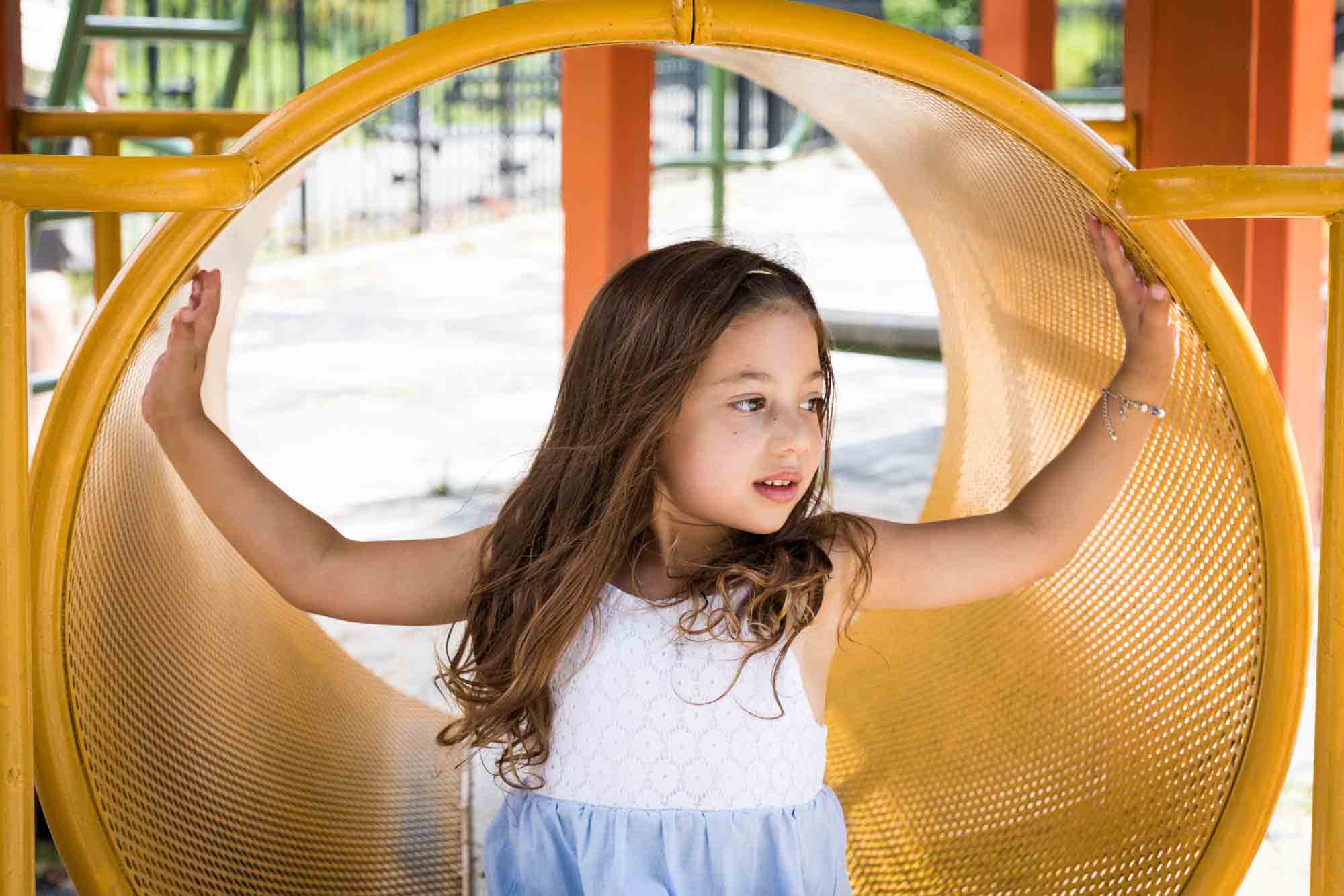 Little girl with arms outstretched on orange tube on playground