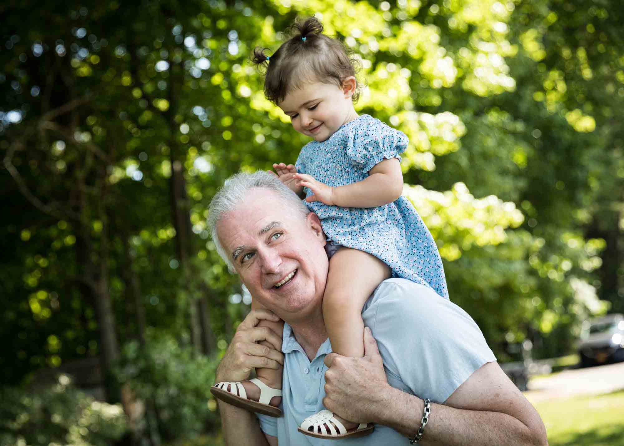 Grandfather holding little girl on his shoulders while she plays with his hair