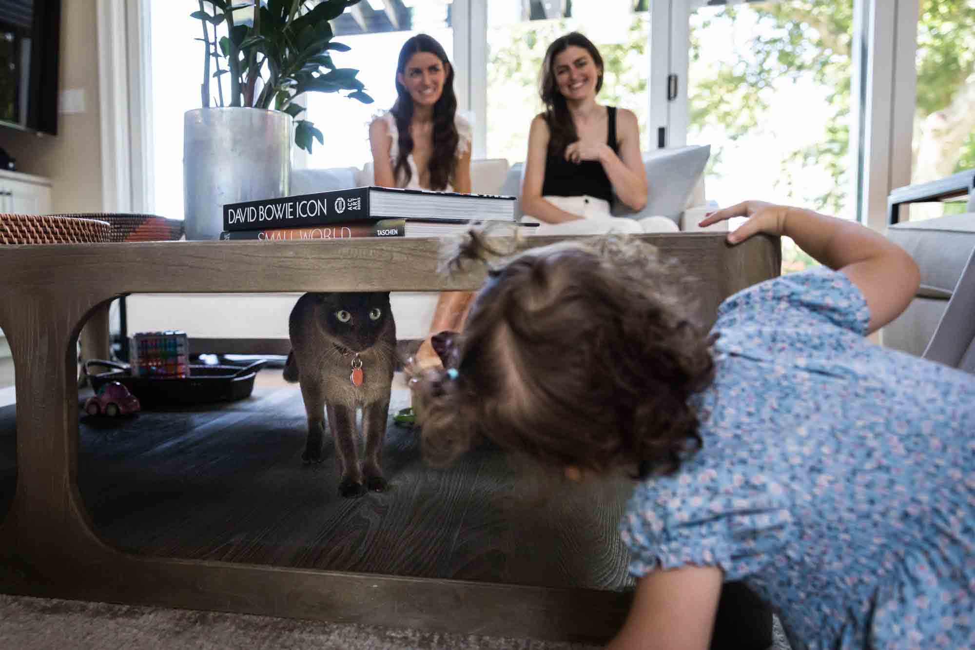 Little girl looking for cat under coffee table for an article advertising family portrait gift certificates