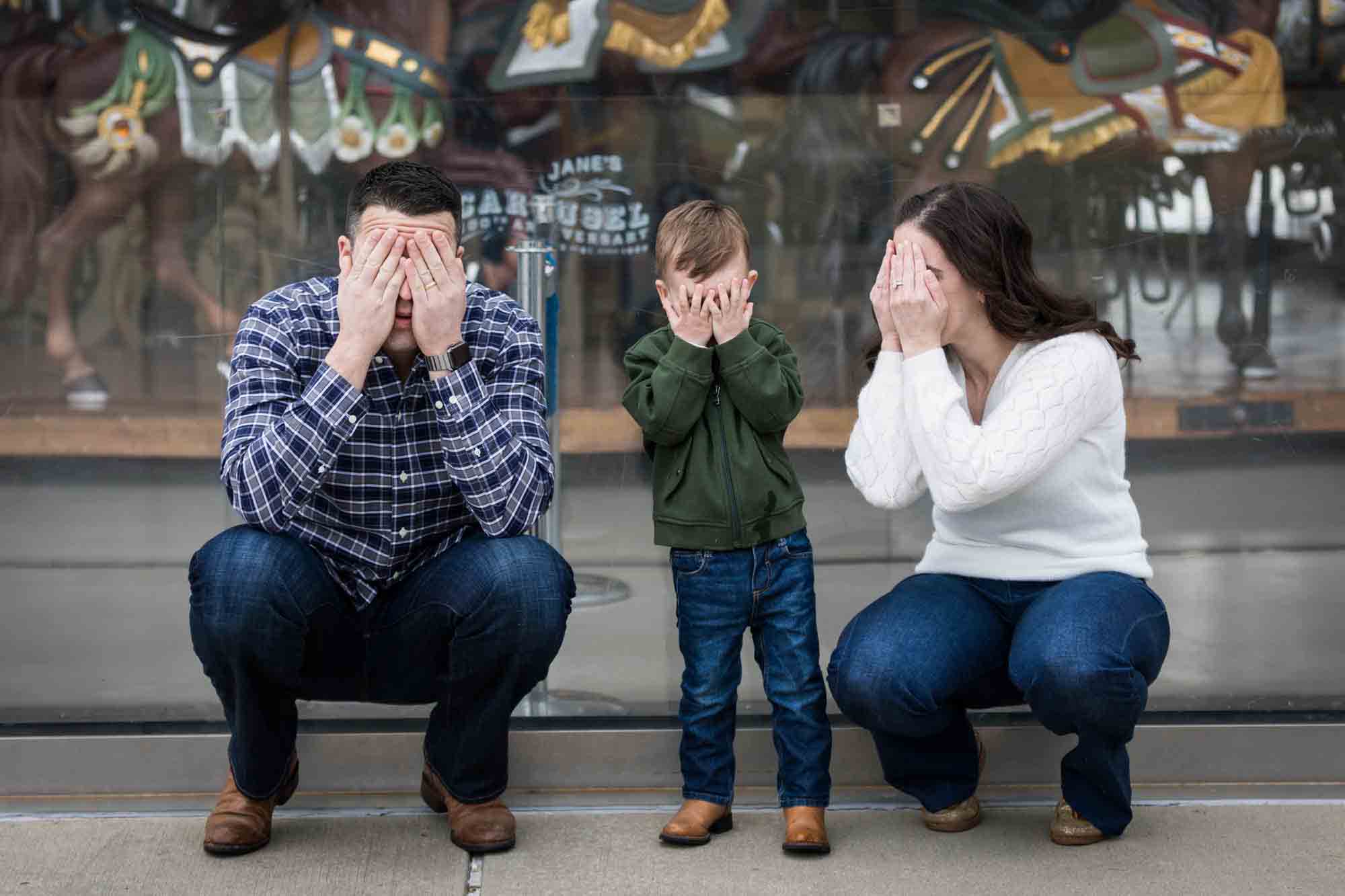 Parents and son playing peek-a-boo in front of carousel for an article advertising family portrait gift certificates