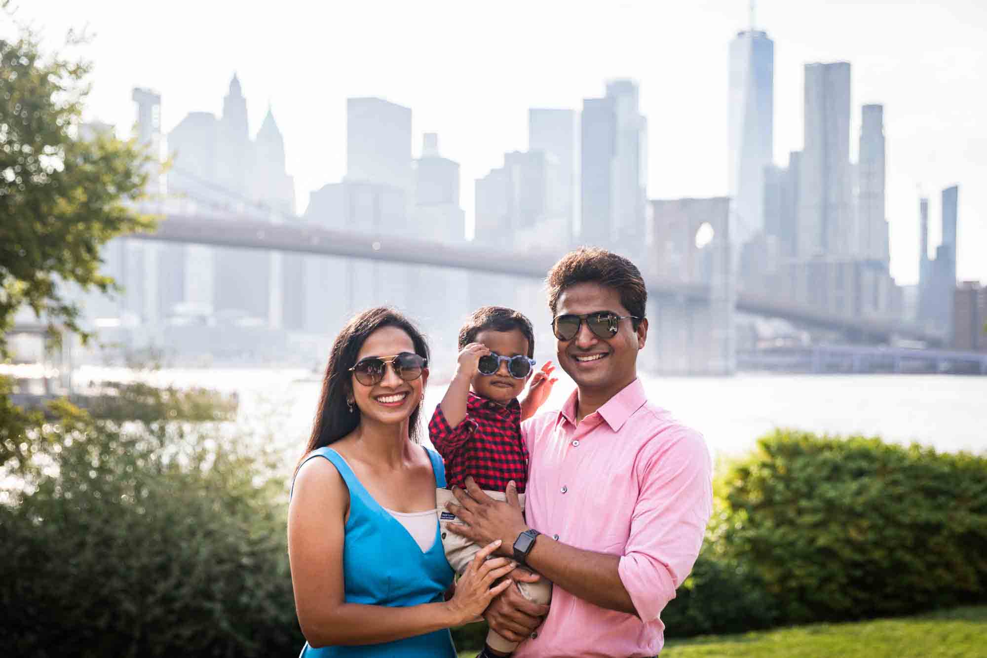 Indian American family holding young son and all wearing sunglasses in front of NYC skyline