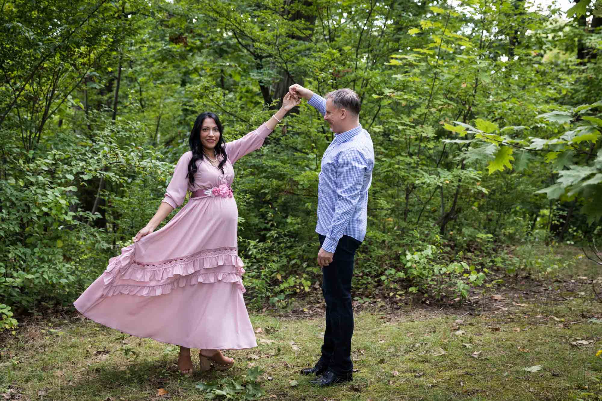 Pregnant woman wearing pink dress dancing with husband in Forest Park