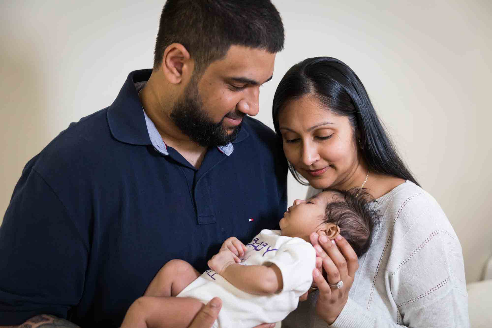 Indian American parents looking down on newborn baby for an article advertising family portrait gift certificates