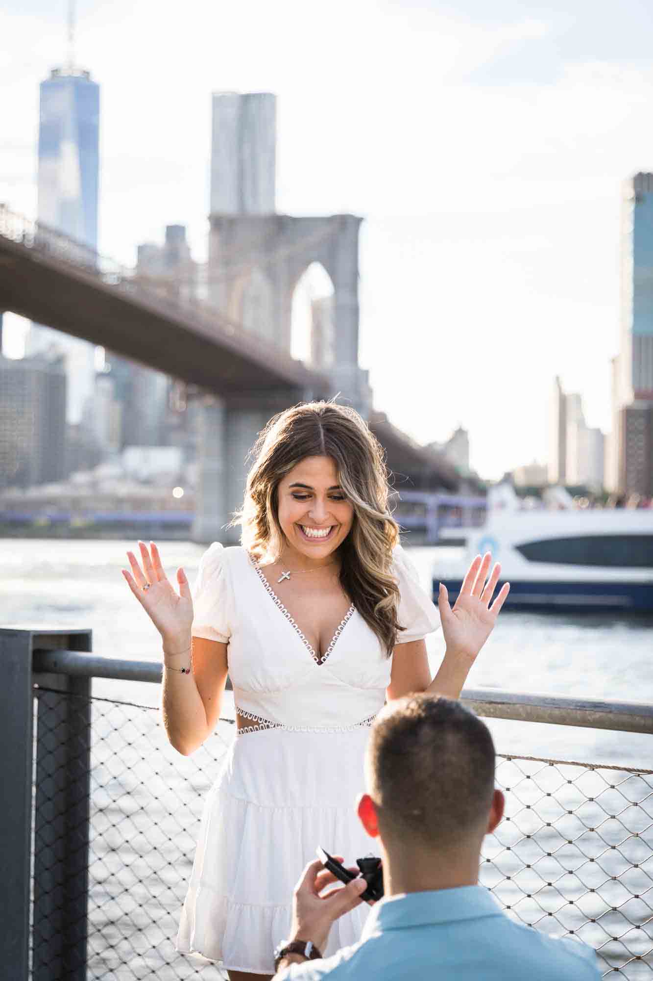 Woman with hands raised reacting excitedly during a Brooklyn Bridge Park surprise proposal
