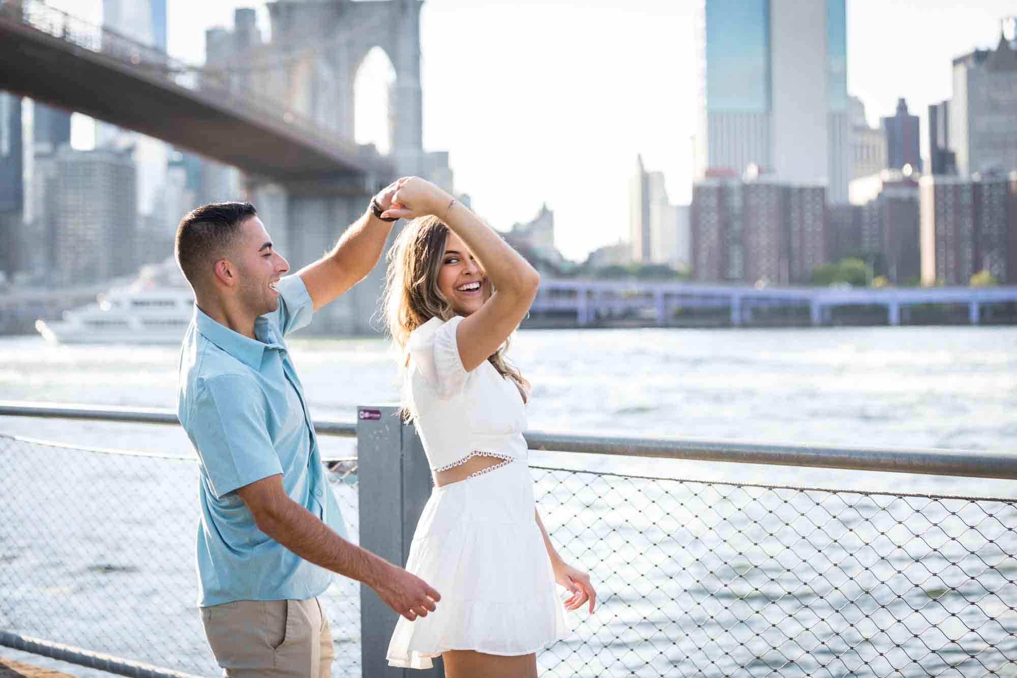 Couple dancing on boardwalk in front of Brooklyn Bridge during a surprise proposal in Brooklyn Bridge Park