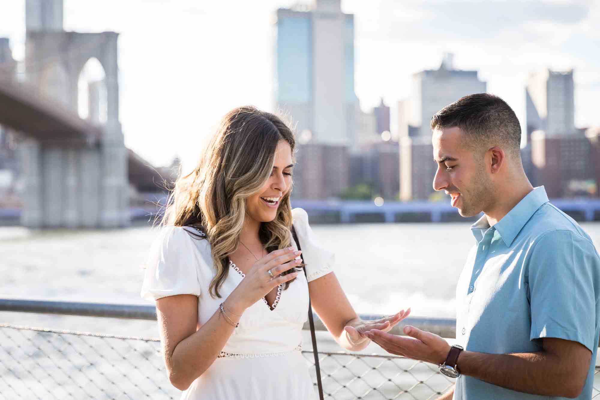 Man putting ring on woman's hand with Brooklyn Bridge in background for an article on how to propose in Brooklyn Bridge Park