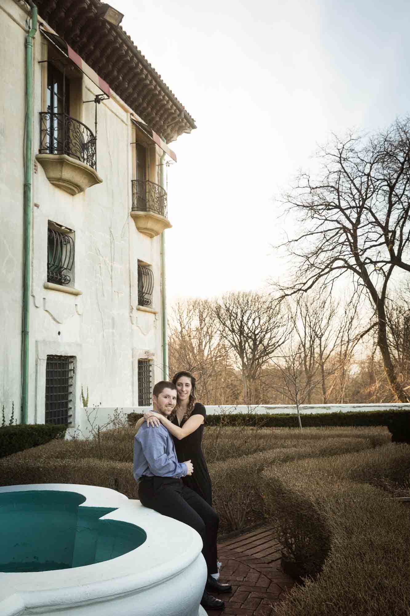 Couple sitting beside fountain in garden at a Vanderbilt Museum engagement photo shoot