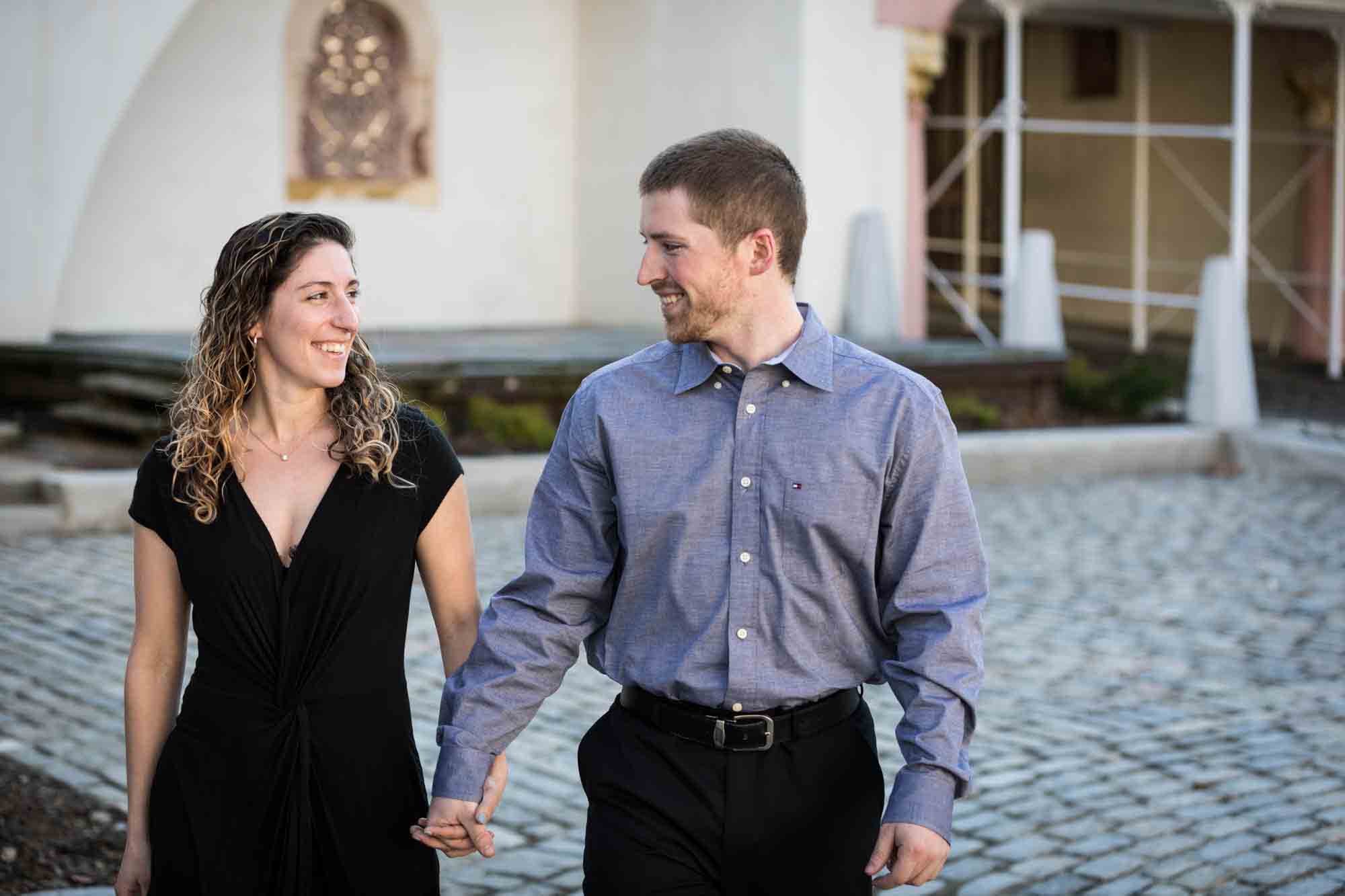 Couple holding hands walking across courtyard during a Vanderbilt Museum engagement photo shoot