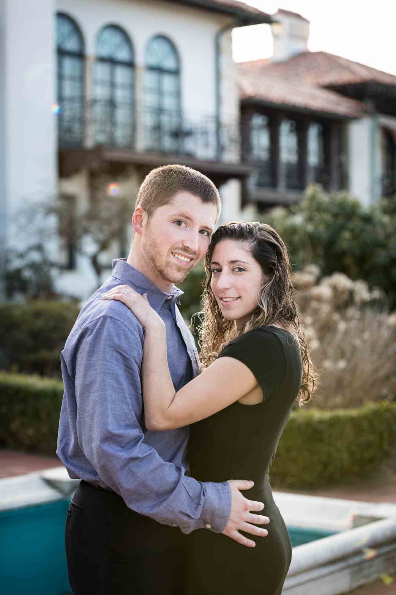 Couple cuddling in front of mansion during a Vanderbilt Museum engagement photo shoot