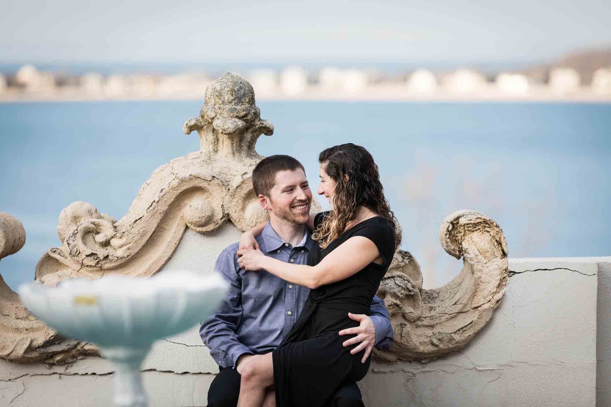 Vanderbilt Museum engagement photo of woman sitting on man's lap with Northport Bay in background