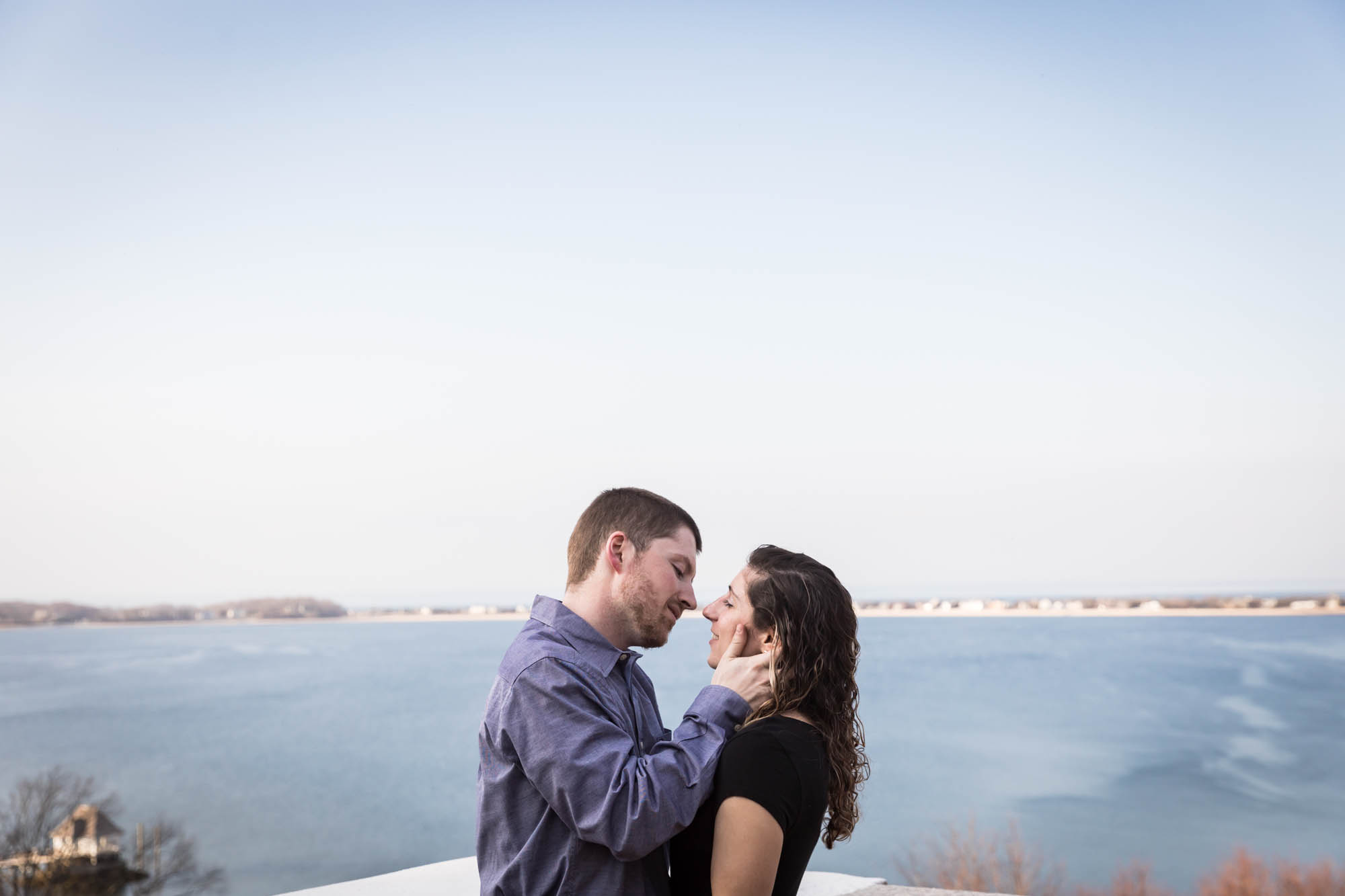 Couple about to kiss in front of Northport Bay during a Vanderbilt Museum engagement photo shoot