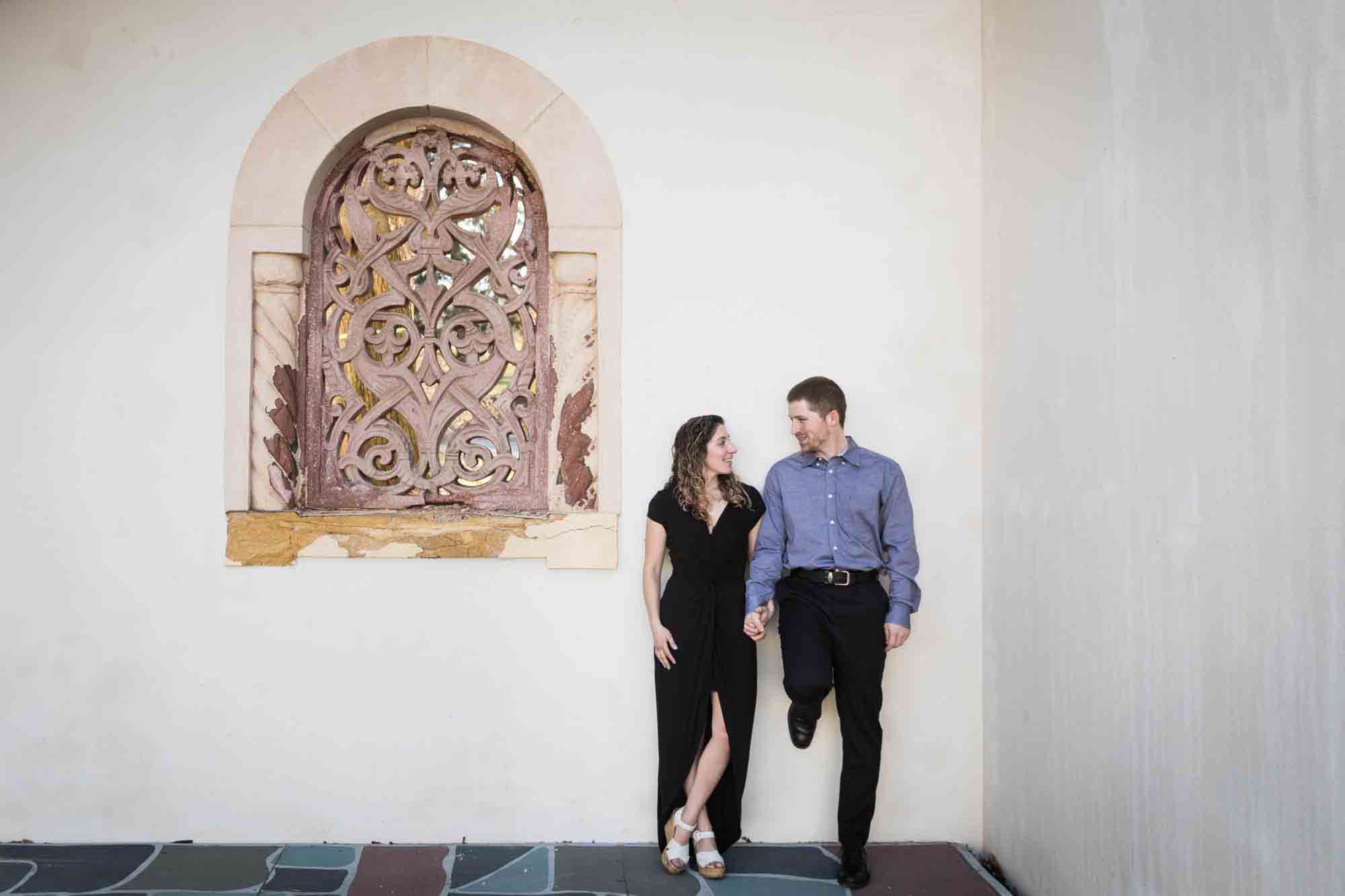 Couple leaning against white wall during a Vanderbilt Museum engagement photo shoot