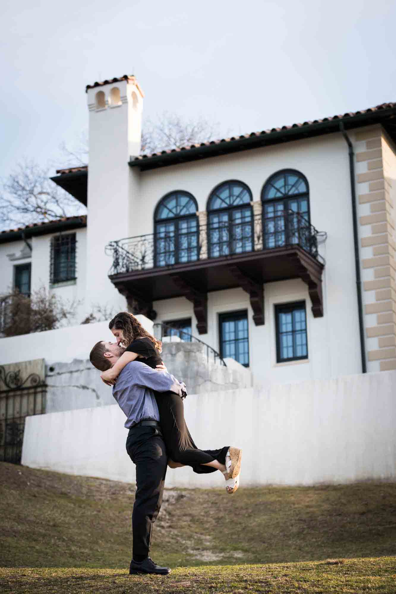 Man lifting woman up in front of building at a Vanderbilt Museum engagement photo shoot