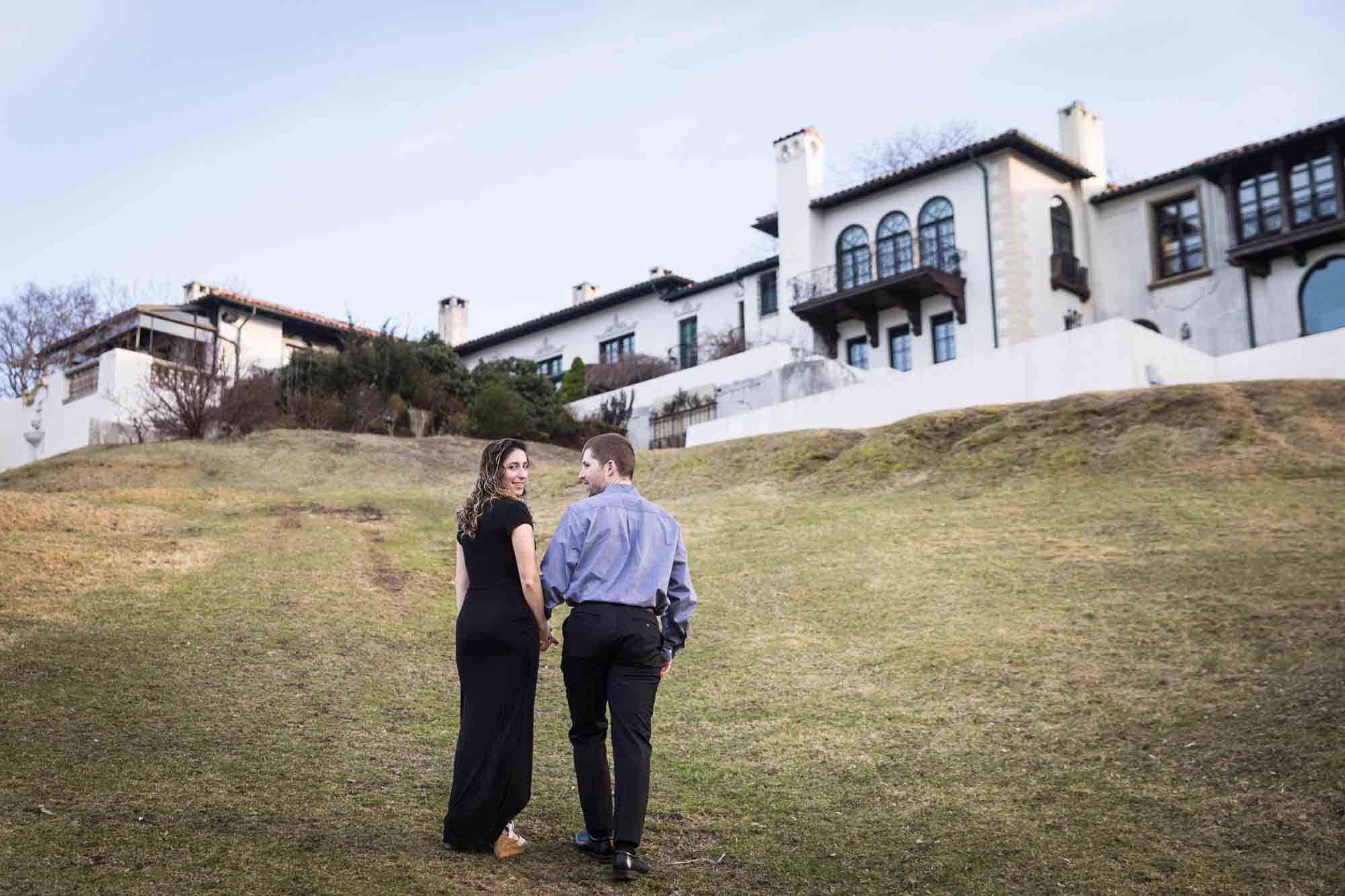 Couple walking up hill in grass to building at a Vanderbilt Museum engagement photo shoot