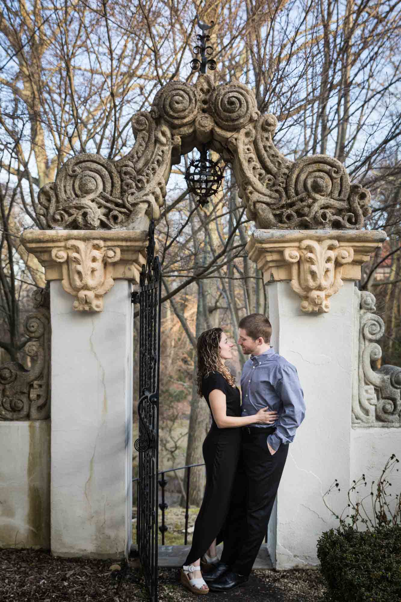 Vanderbilt Museum engagement photos of couple cuddling under intricate stone gate