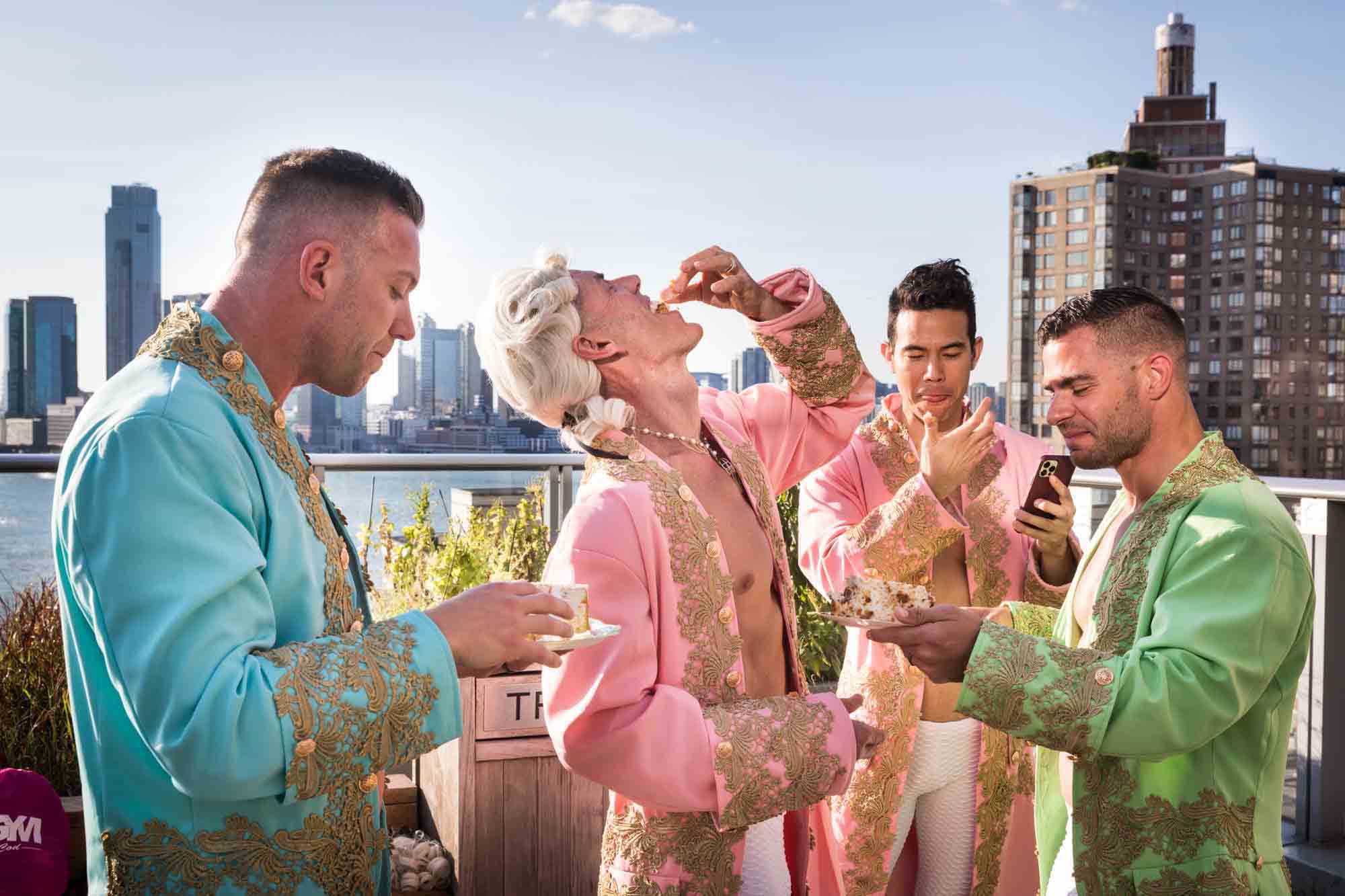 Men dressed as French courtiers eating cake with NYC waterfront in background