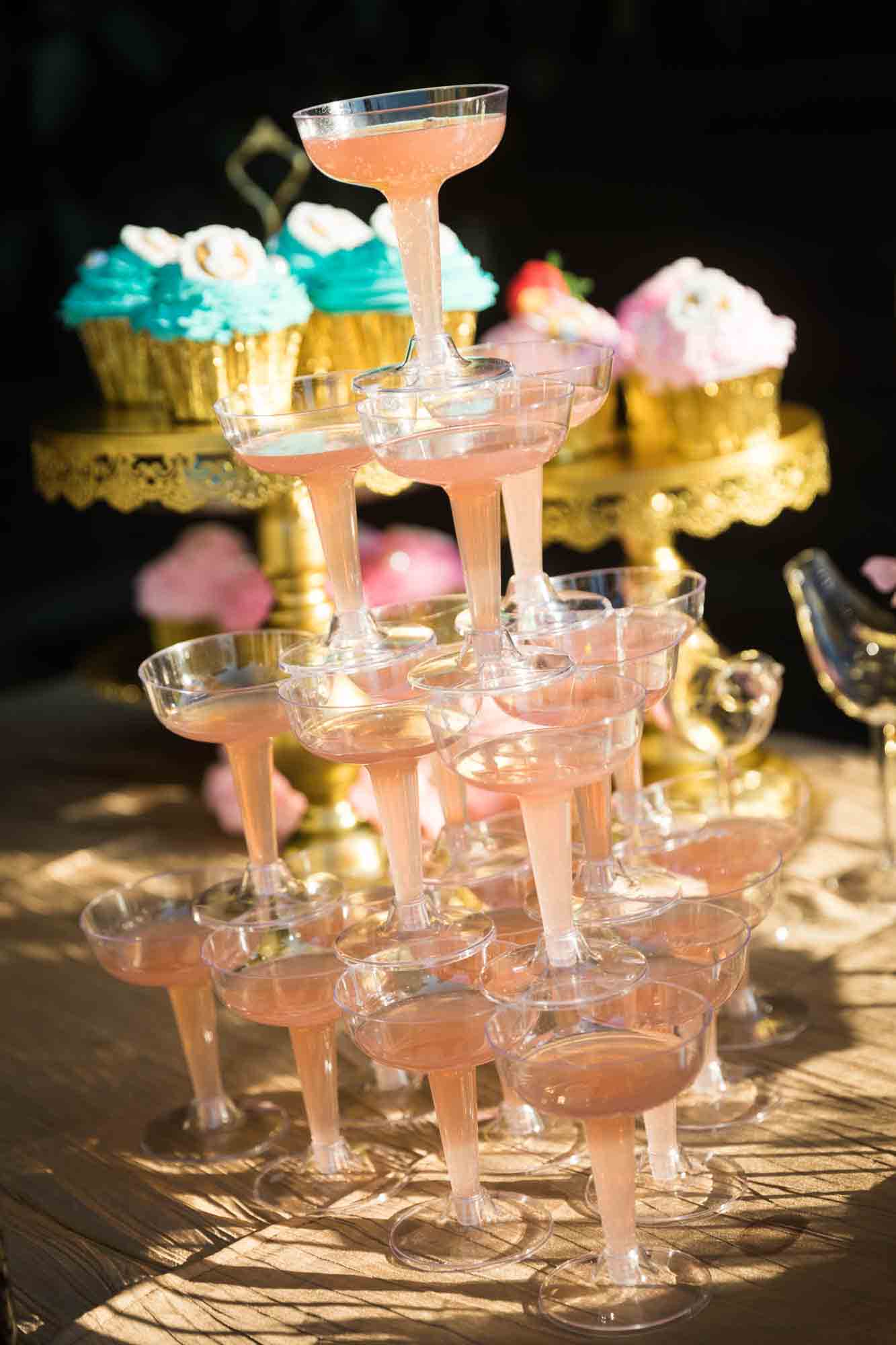 Tower of champagne glasses filled with pink champagne in front of elaborate desserts