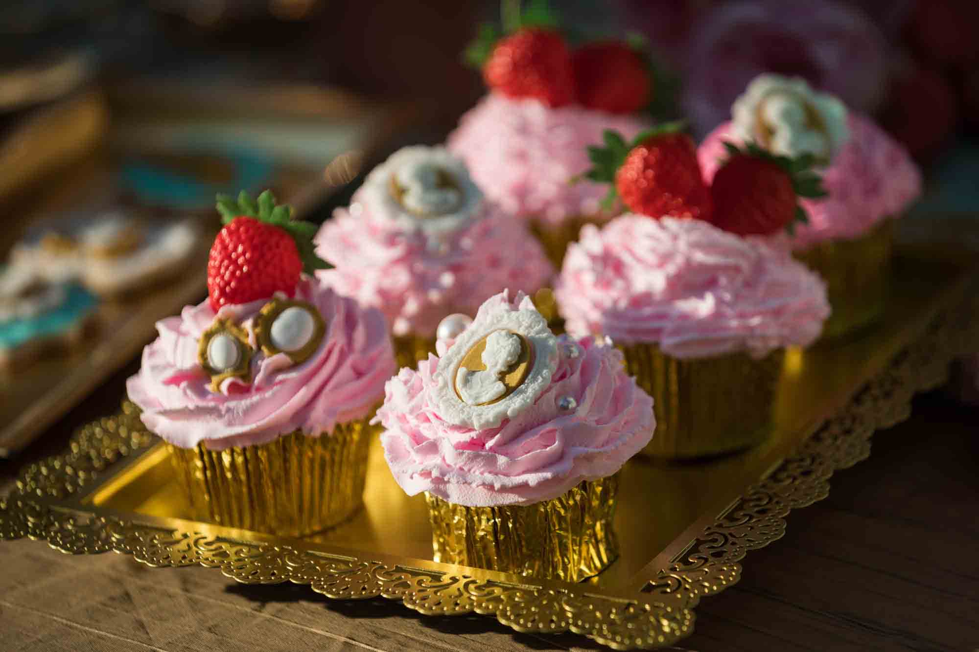 Pink frosted cupcakes with gold wrappers on a gold tray