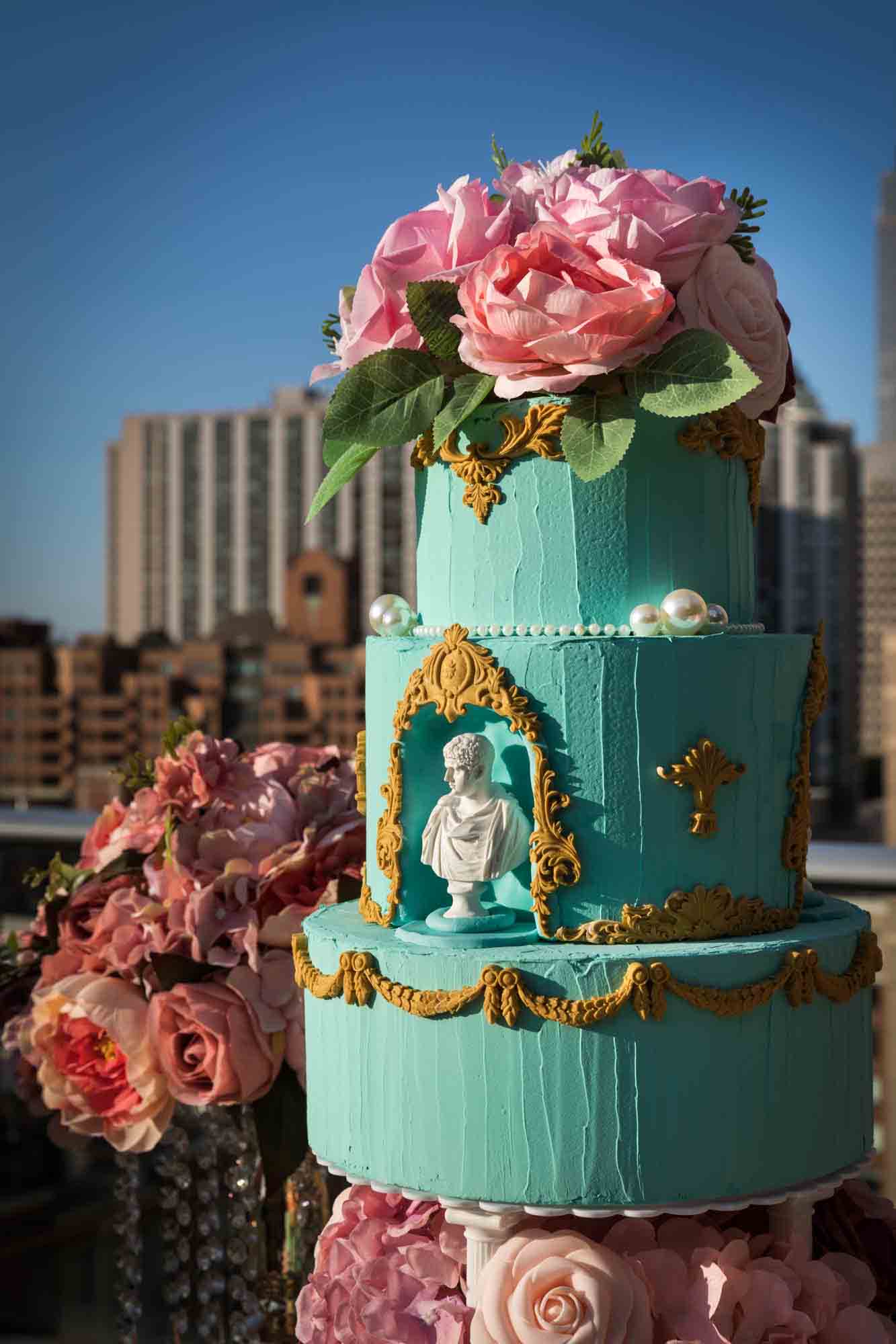 A three-tiered cake with aqua frosting and pink flowers on top