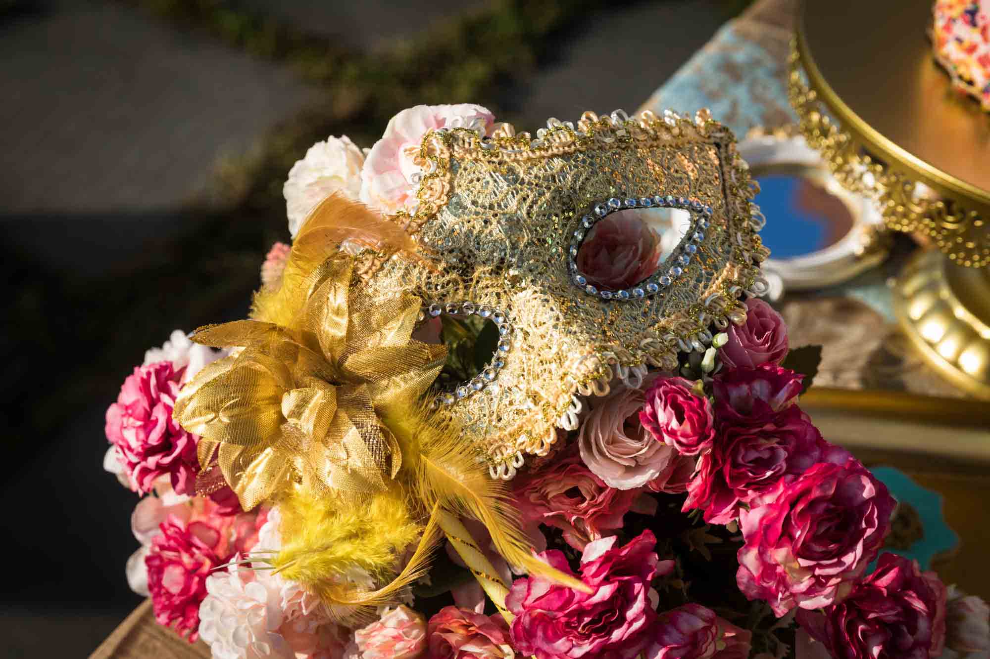 Gold, elaborate mask resting on bed of pink flowers