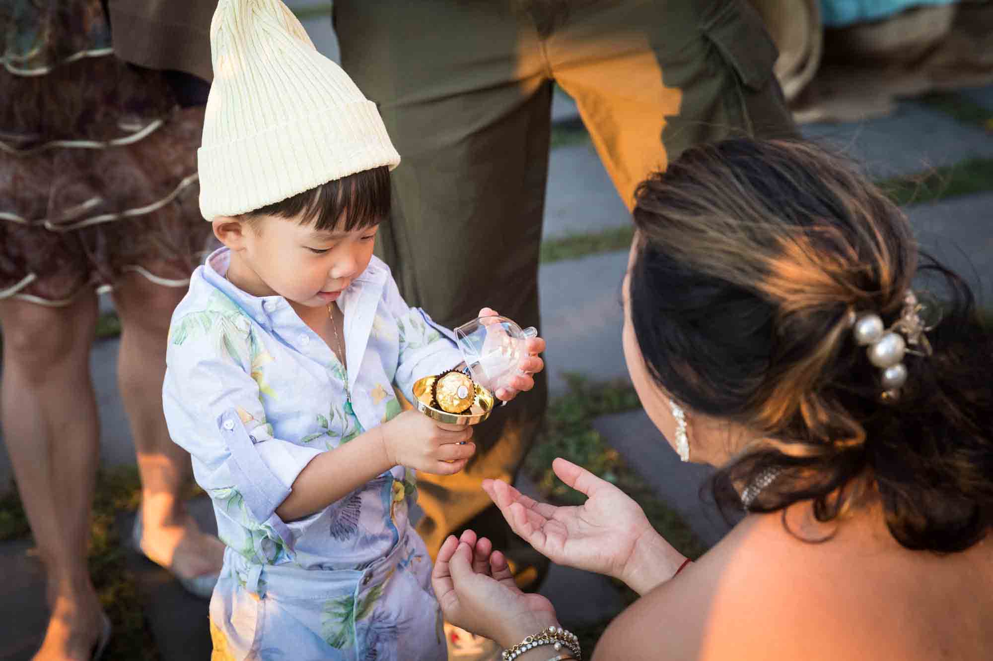 Hostess presenting a dome-covered, gold candy to a little boy wearing a cap