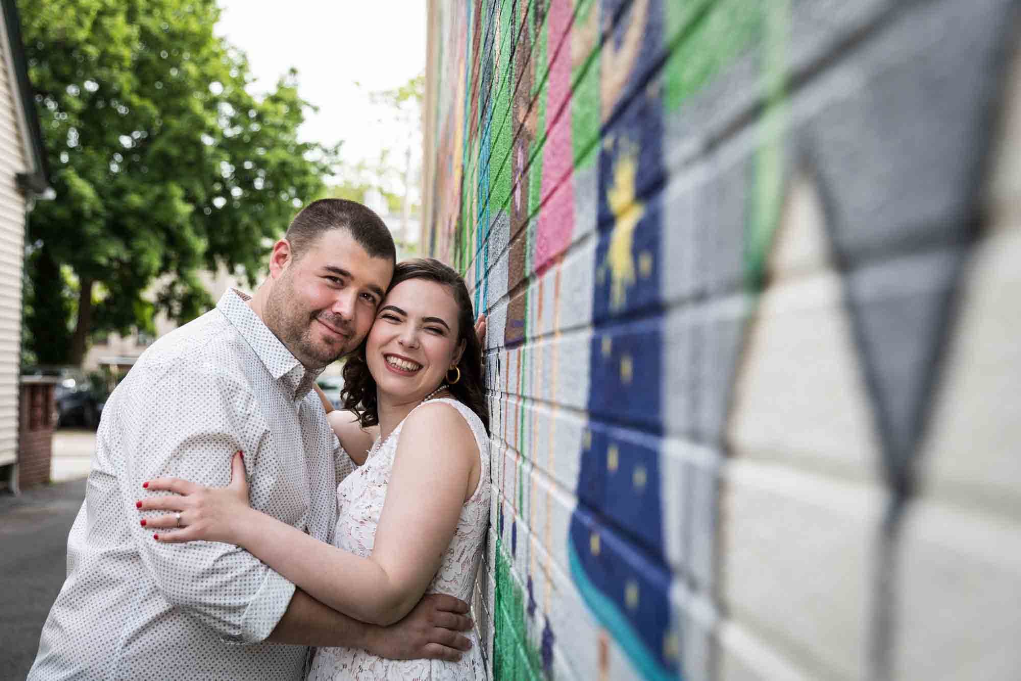 Couple hugging in front of colorful wall mural for an article on how to recreate your love story in your engagement shoot