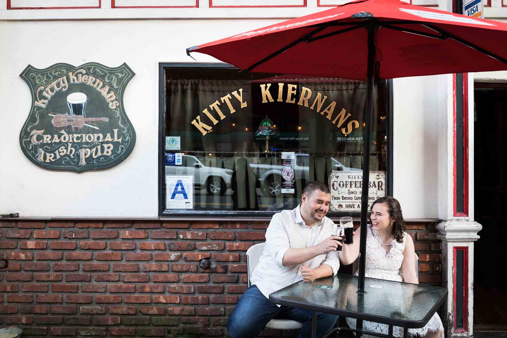 Couple toasting glasses of beer in front of Irish bar for an article on how to recreate your love story in your engagement shoot