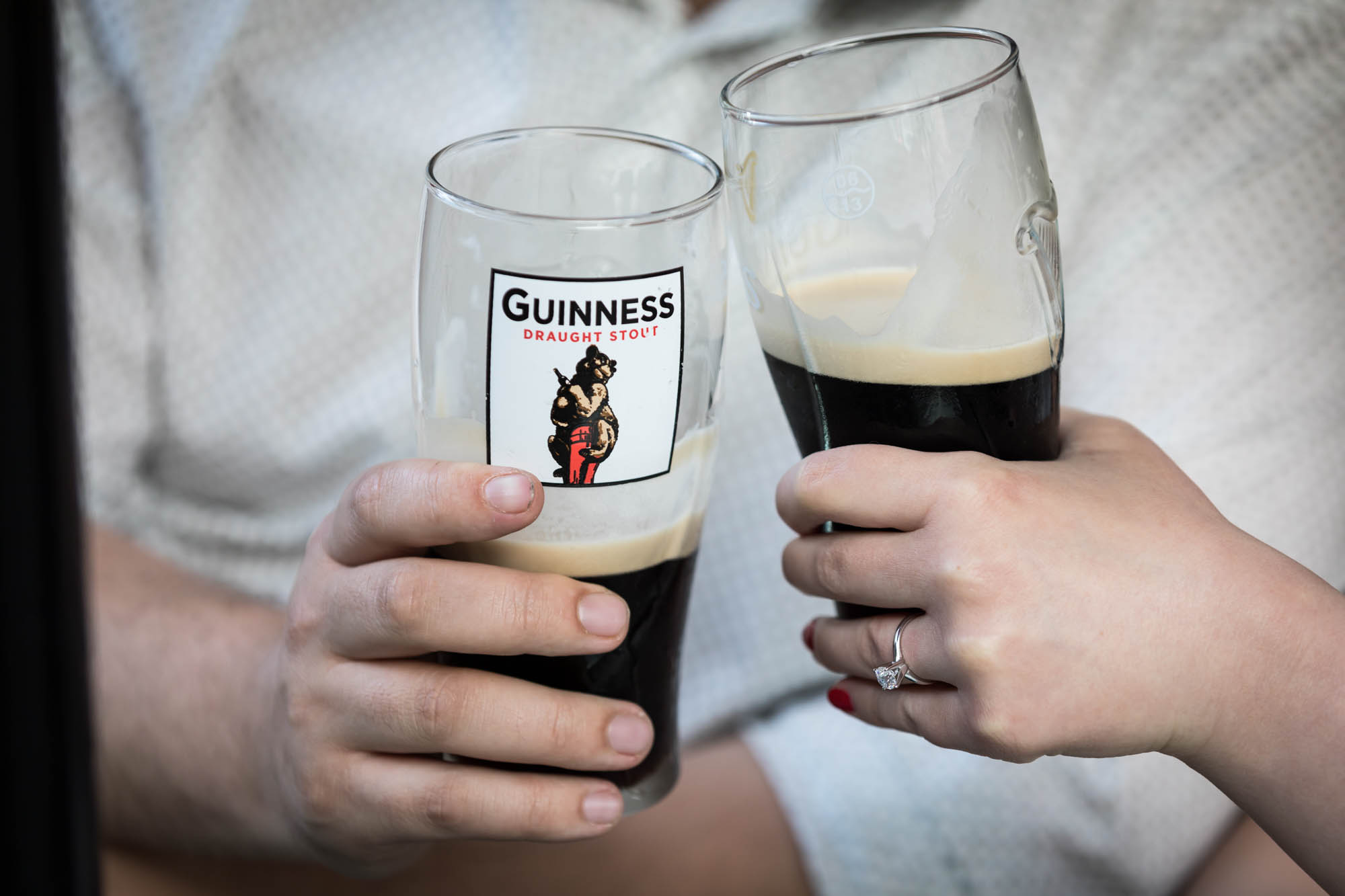 Hands holding glasses of dark beer for an article on how to recreate your love story in your engagement shoot