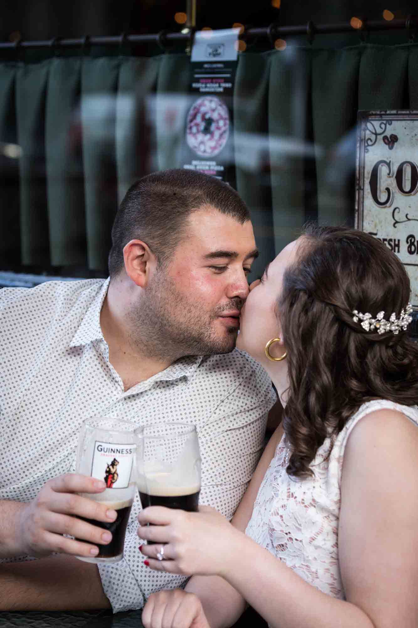 Couple kissing while holding glasses of beer for an article on how to recreate your love story in your engagement shoot