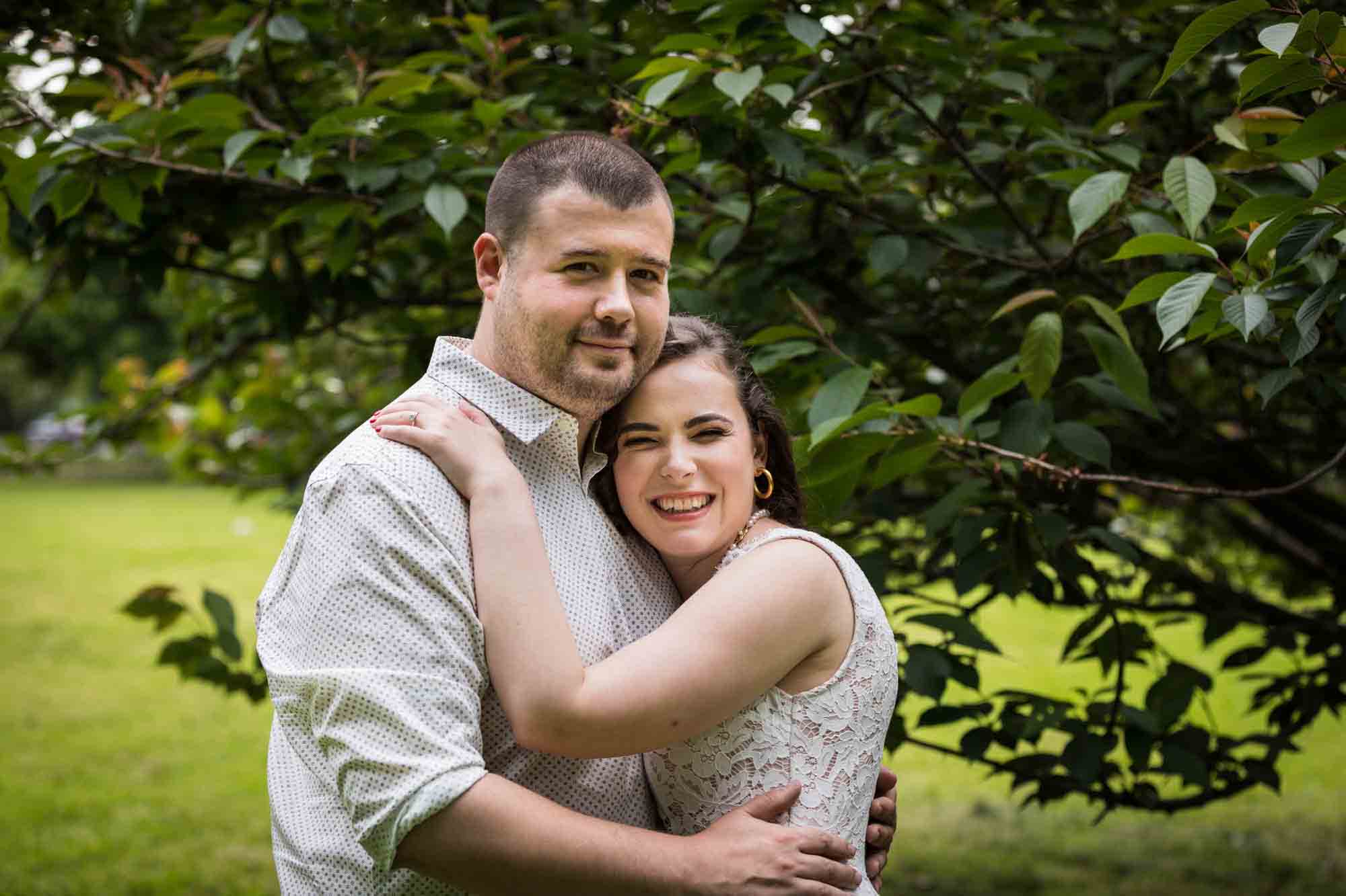 Couple hugging in front of tree for an article on how to recreate your love story in your engagement shoot