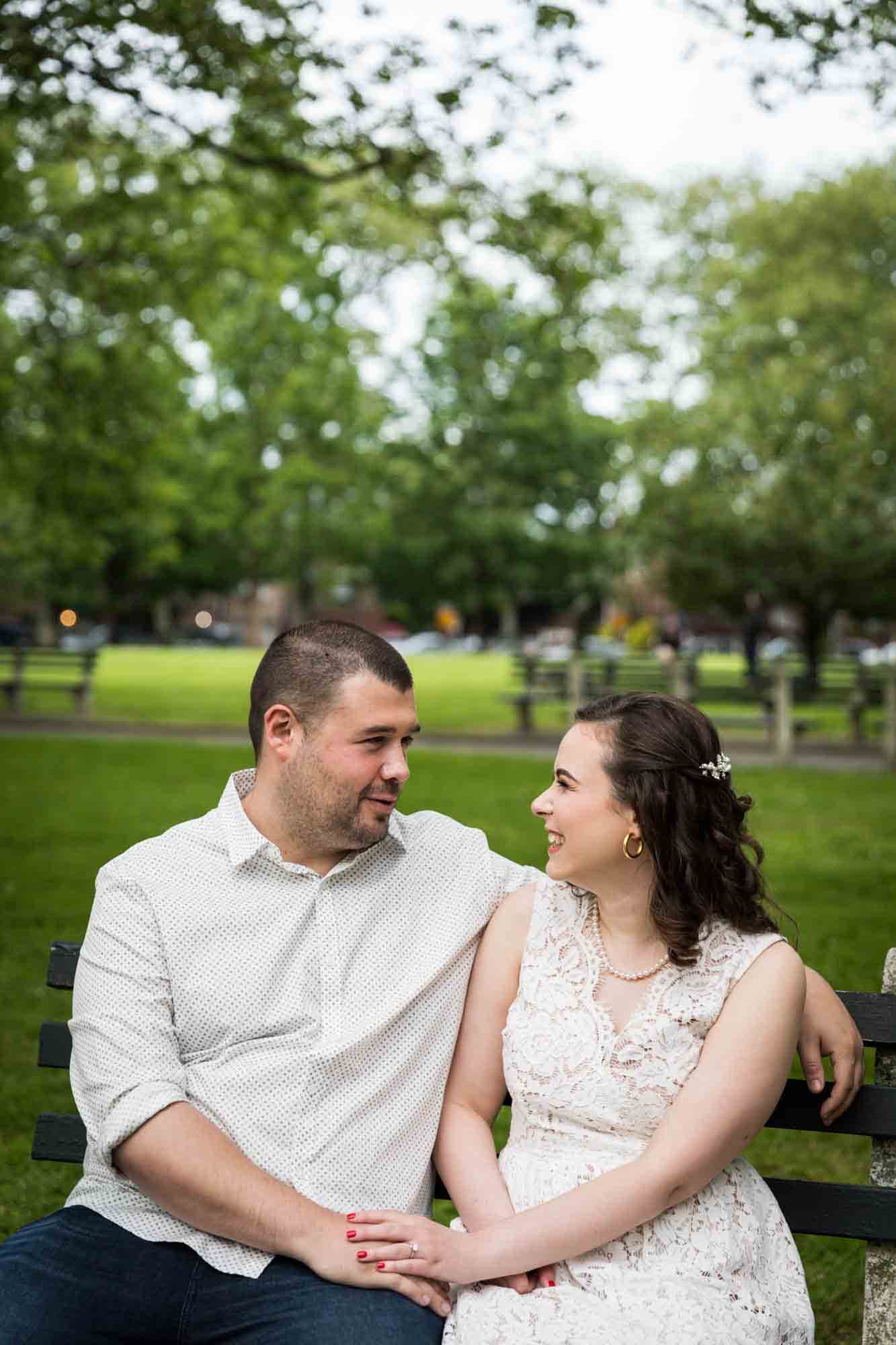 Couple sitting on bench looking at each other during a Dyker Heights engagement shoot