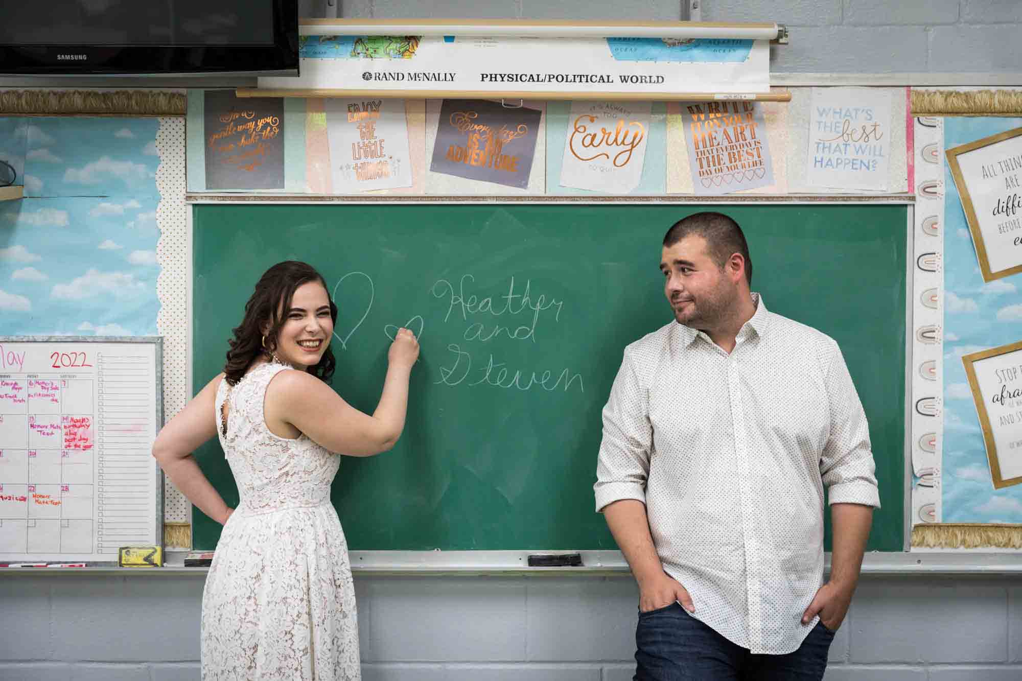 Couple standing in front of chalkboard as woman writes on board for an article on how to recreate your love story in your engagement shoot