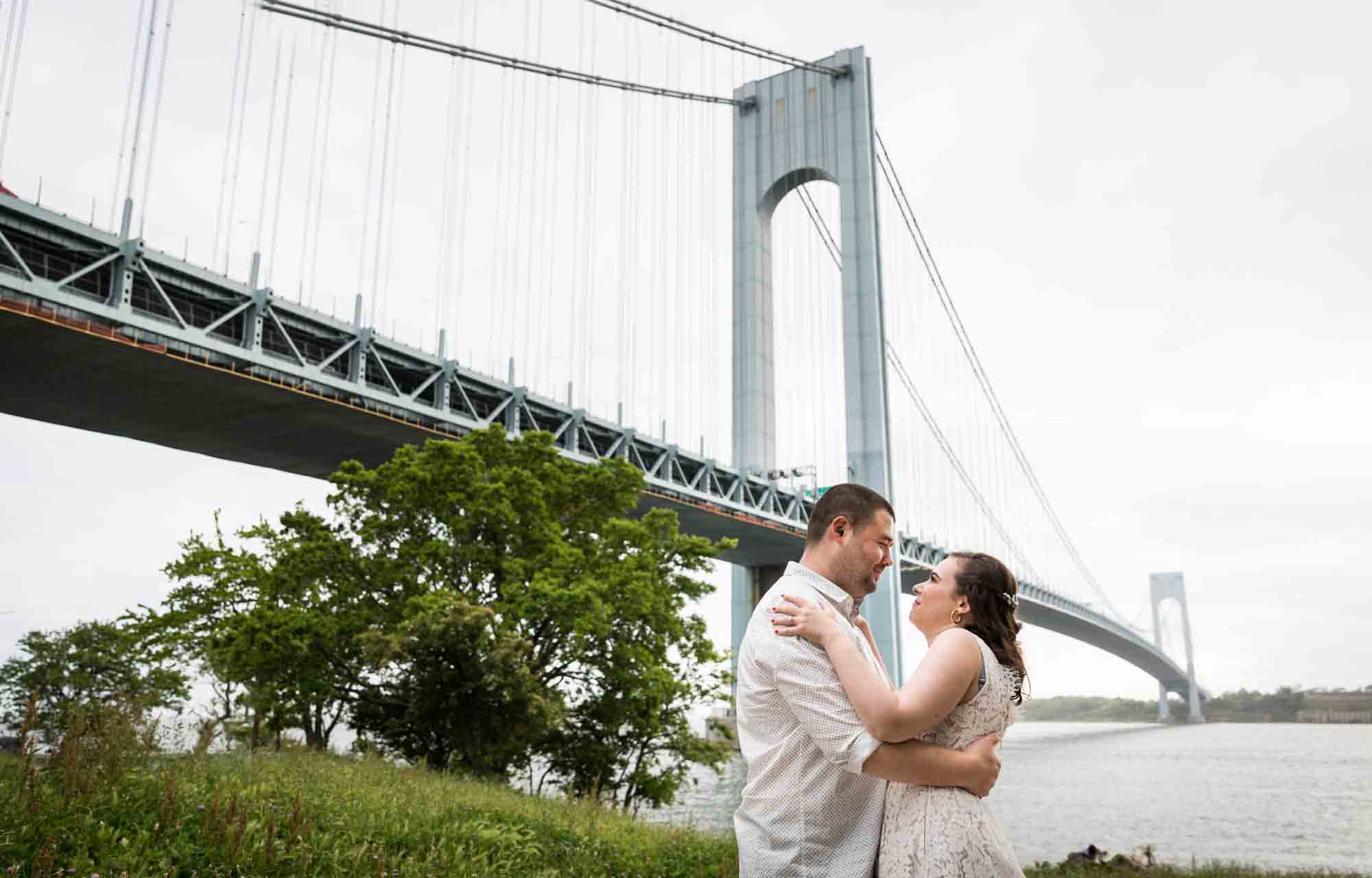 Couple hugging in front of Verrazano Bridge during a Dyker Heights engagement shoot