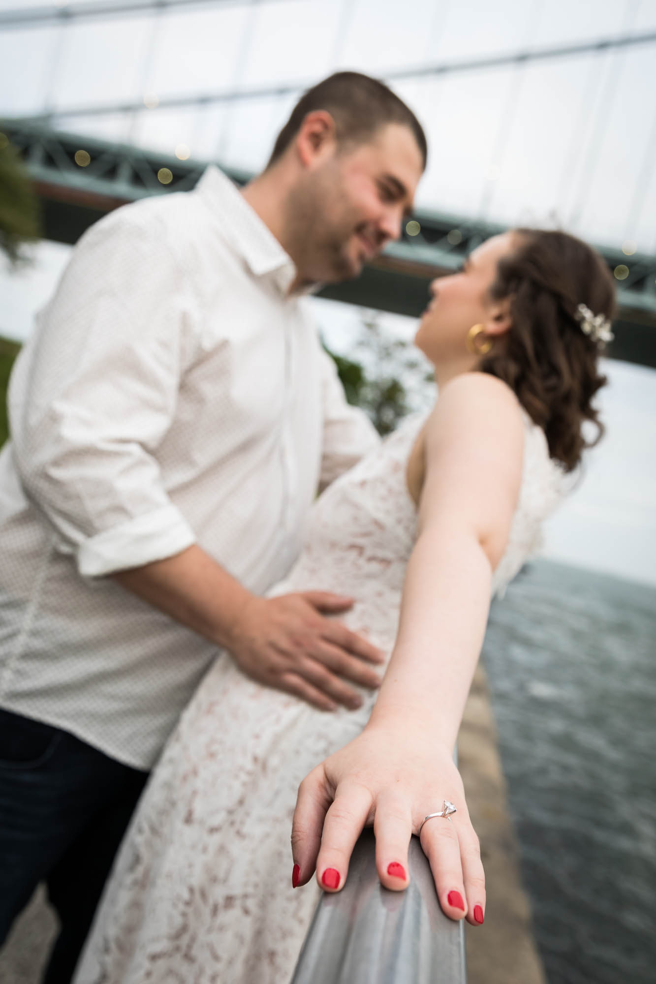 Couple leaning against railing with woman's hand wearing engagement ring in front during a Dyker Heights engagement shoot
