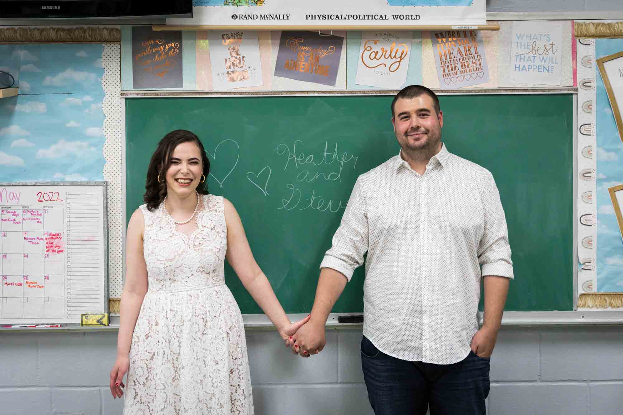 Couple holding hands in front of chalkboard for an article on how to recreate your love story in your engagement shoot