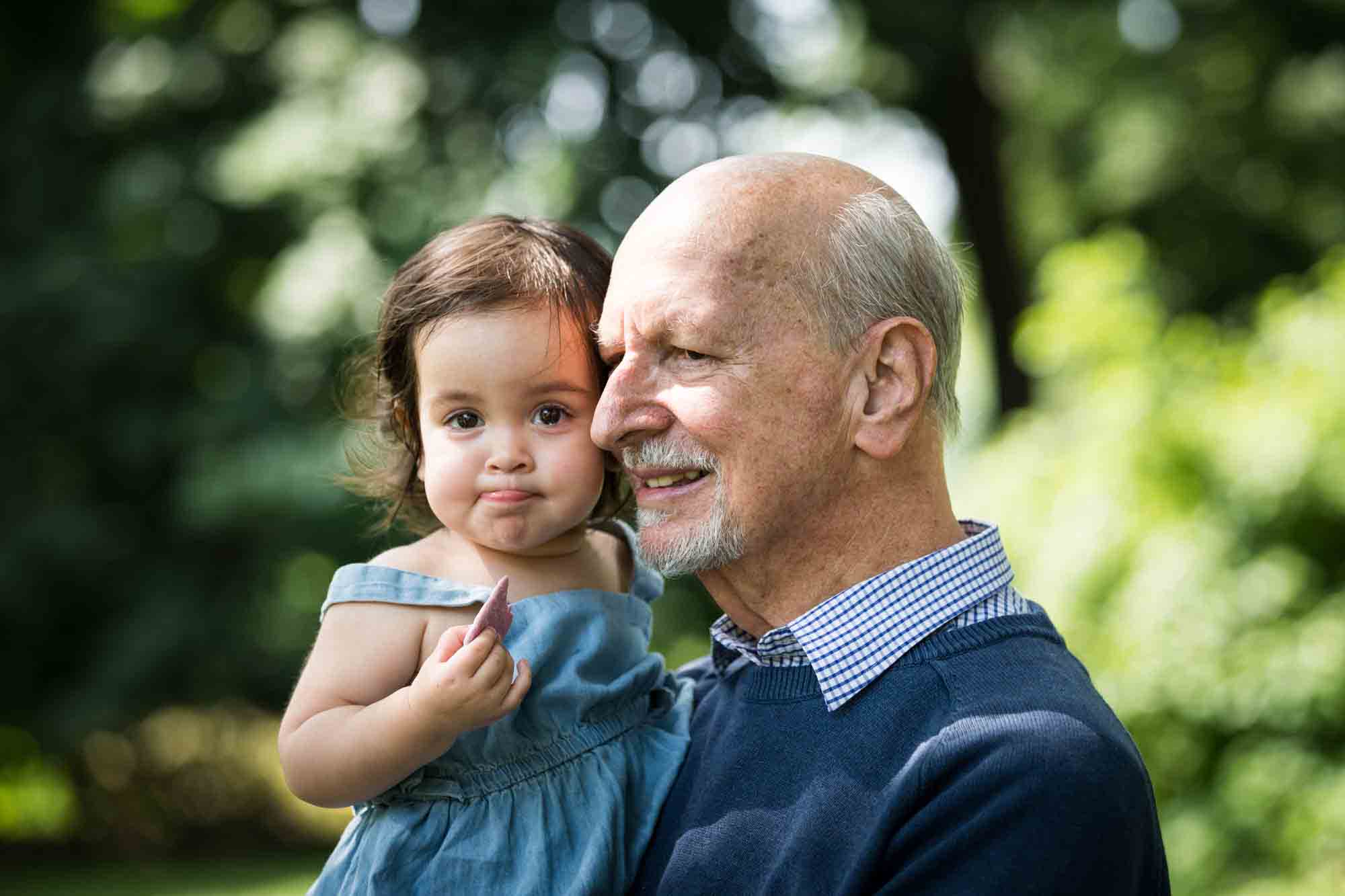 Grandfather holding little girl wearing blue playsuit during a Fort Greene Park family portrait