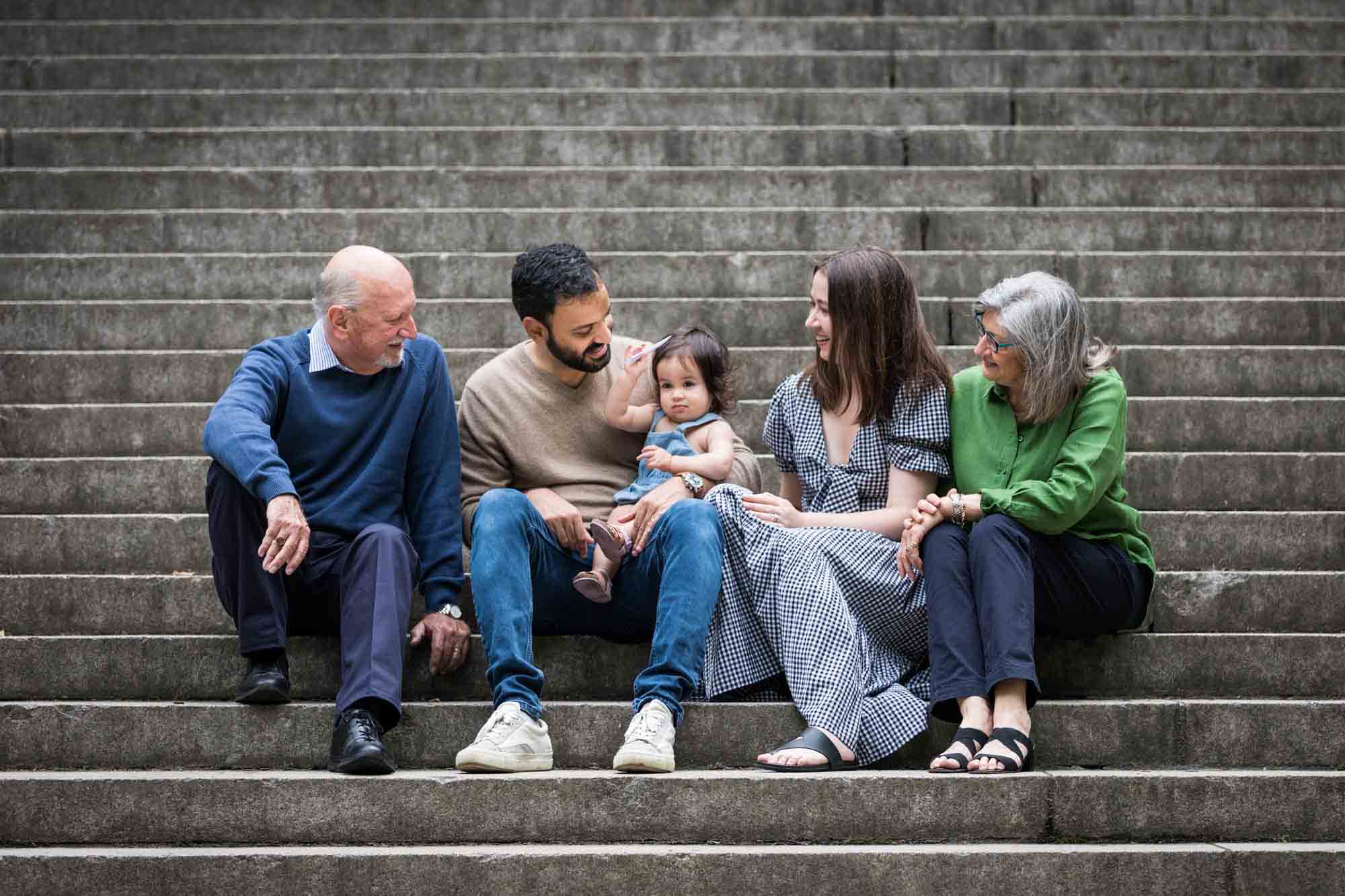 Parents and grandparents focused on toddler while sitting on steps during a Fort Green Park family photo shoot