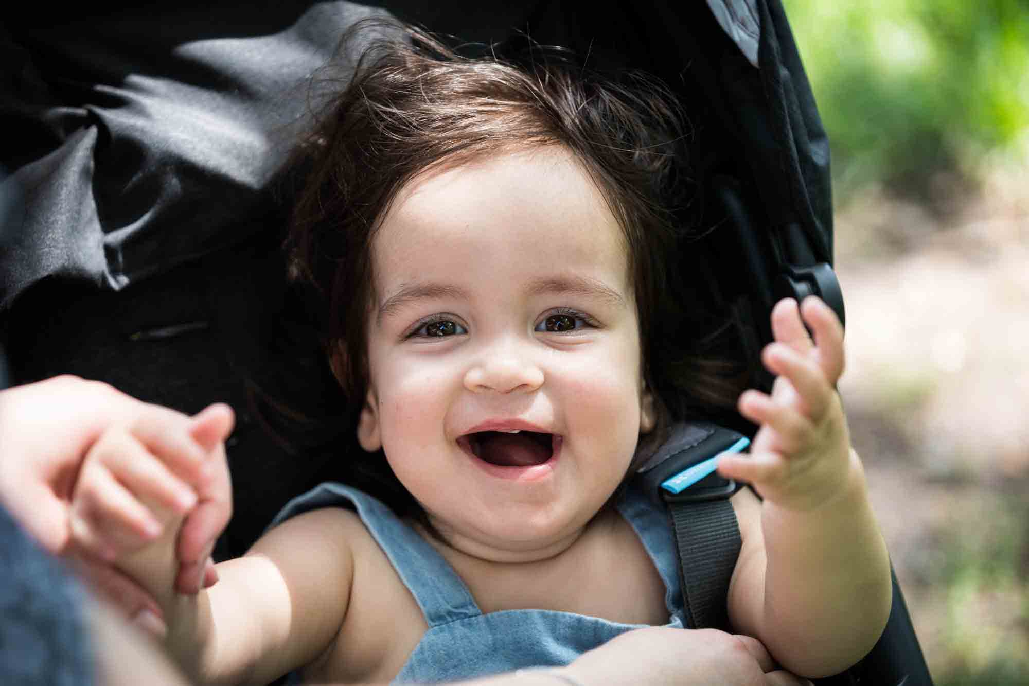 Toddler in stroller with hands outstretched during a Fort Greene Park family portrait