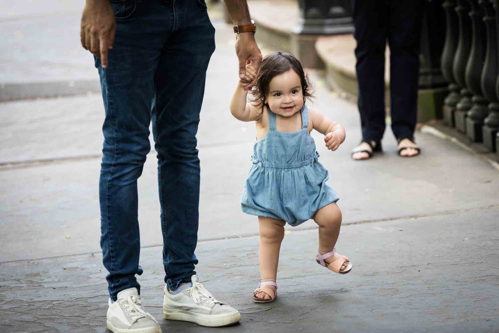 Little girl holding father's hands walking on sidewalk during a Fort Greene Park family portrait