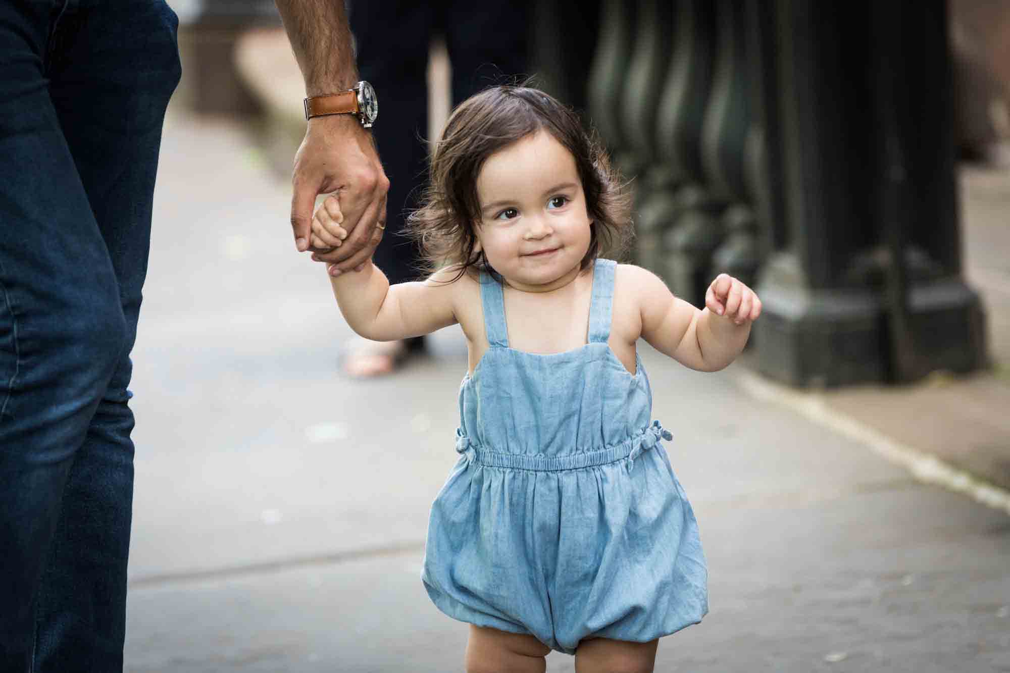 Baby girl wearing a blue playsuit holding a man's hand for an article on how to solve family portrait challenges
