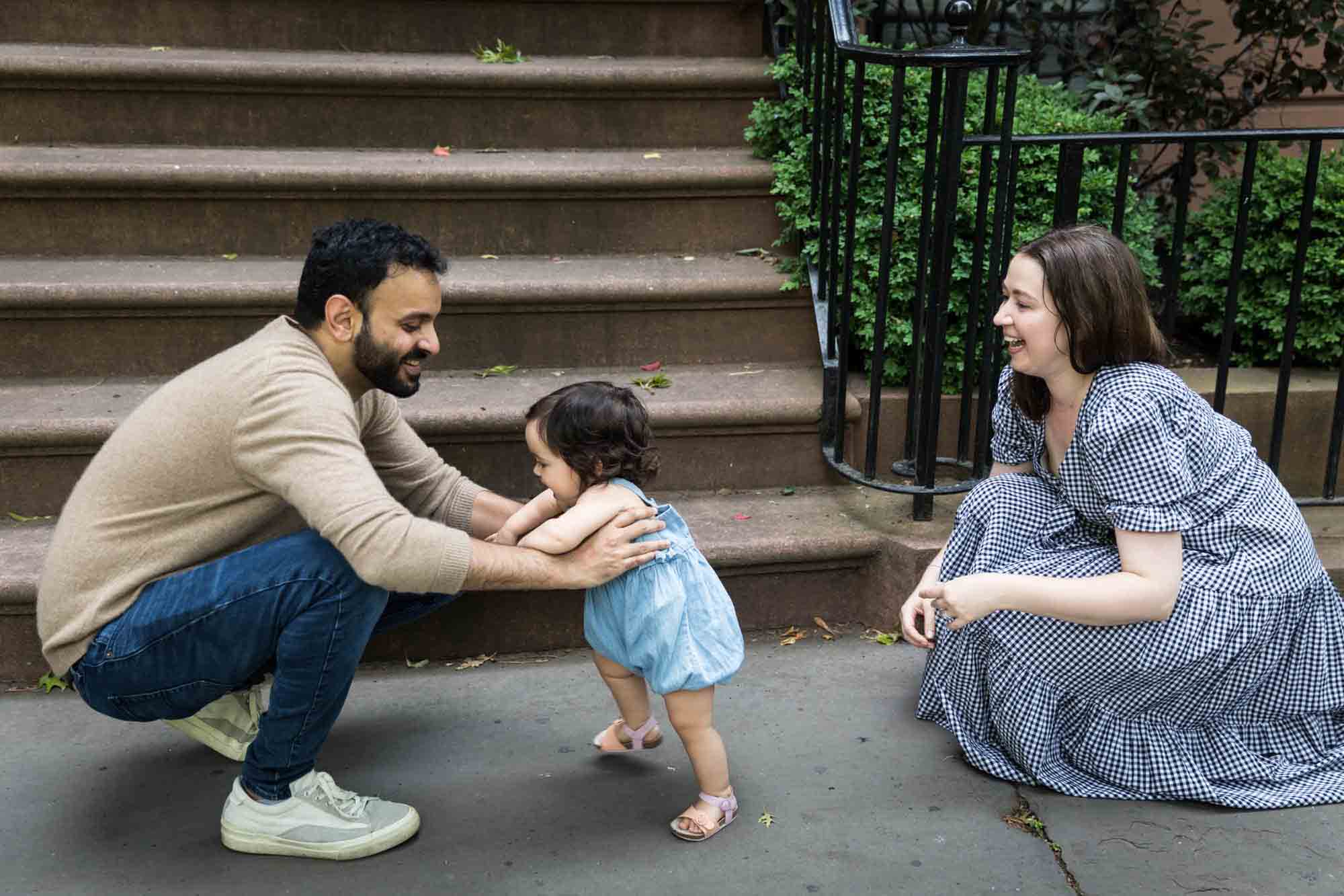 Mother watching as toddler walks to father on sidewalk during a Fort Greene Park family portrait