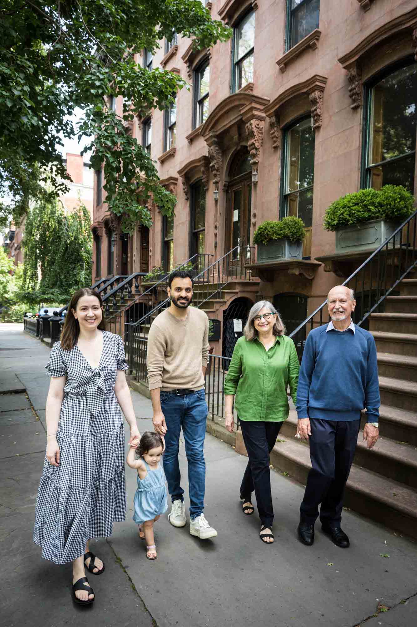 Parents and grandparents walking down sidewalk with toddler during a Fort Greene Park family portrait