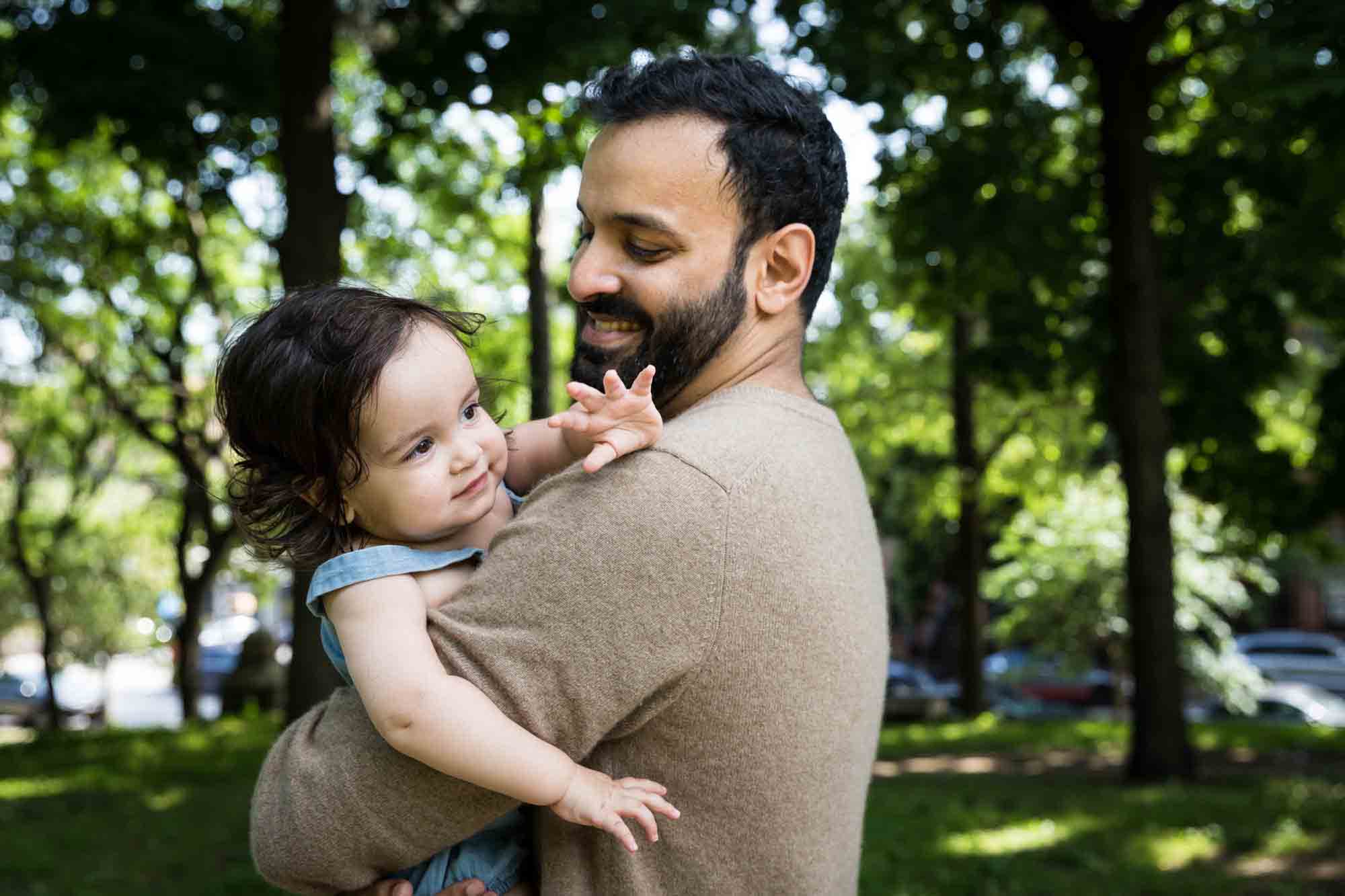 Father holding toddler looking over his shoulder during a Fort Greene Park family portrait