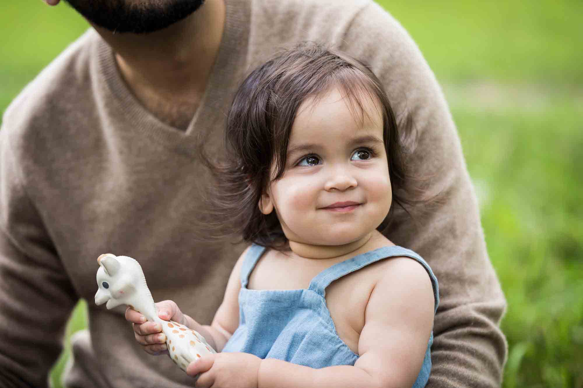 A little girl holding a toy giraffe in her father's arms for an article on how to solve family portrait challenges