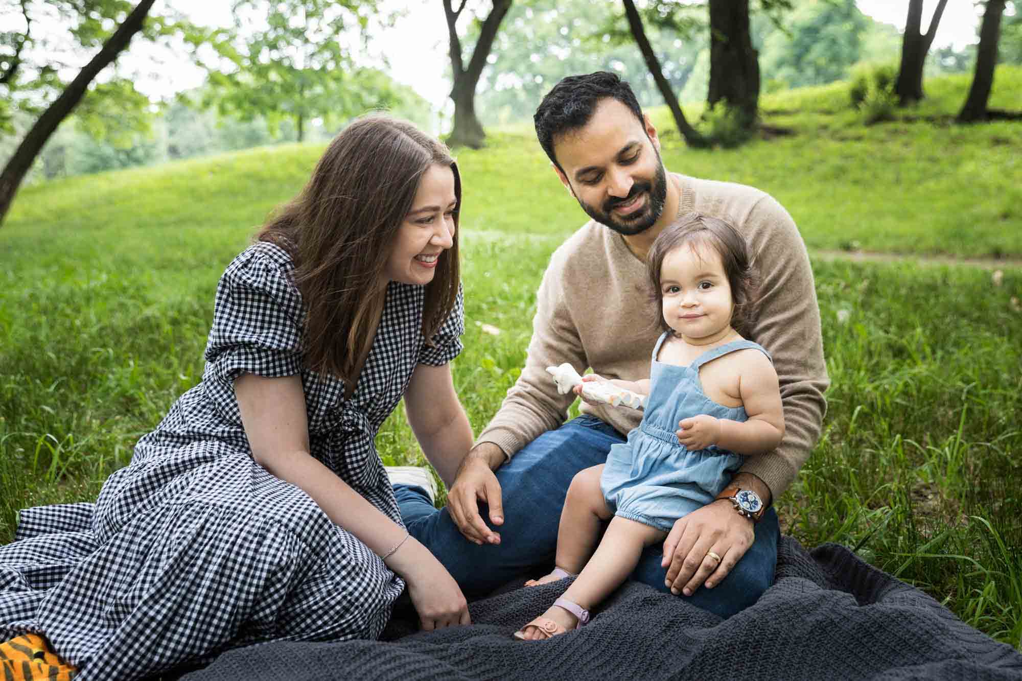 Parents and toddler sitting on a gray blanket during a Fort Green Park family photo shoot