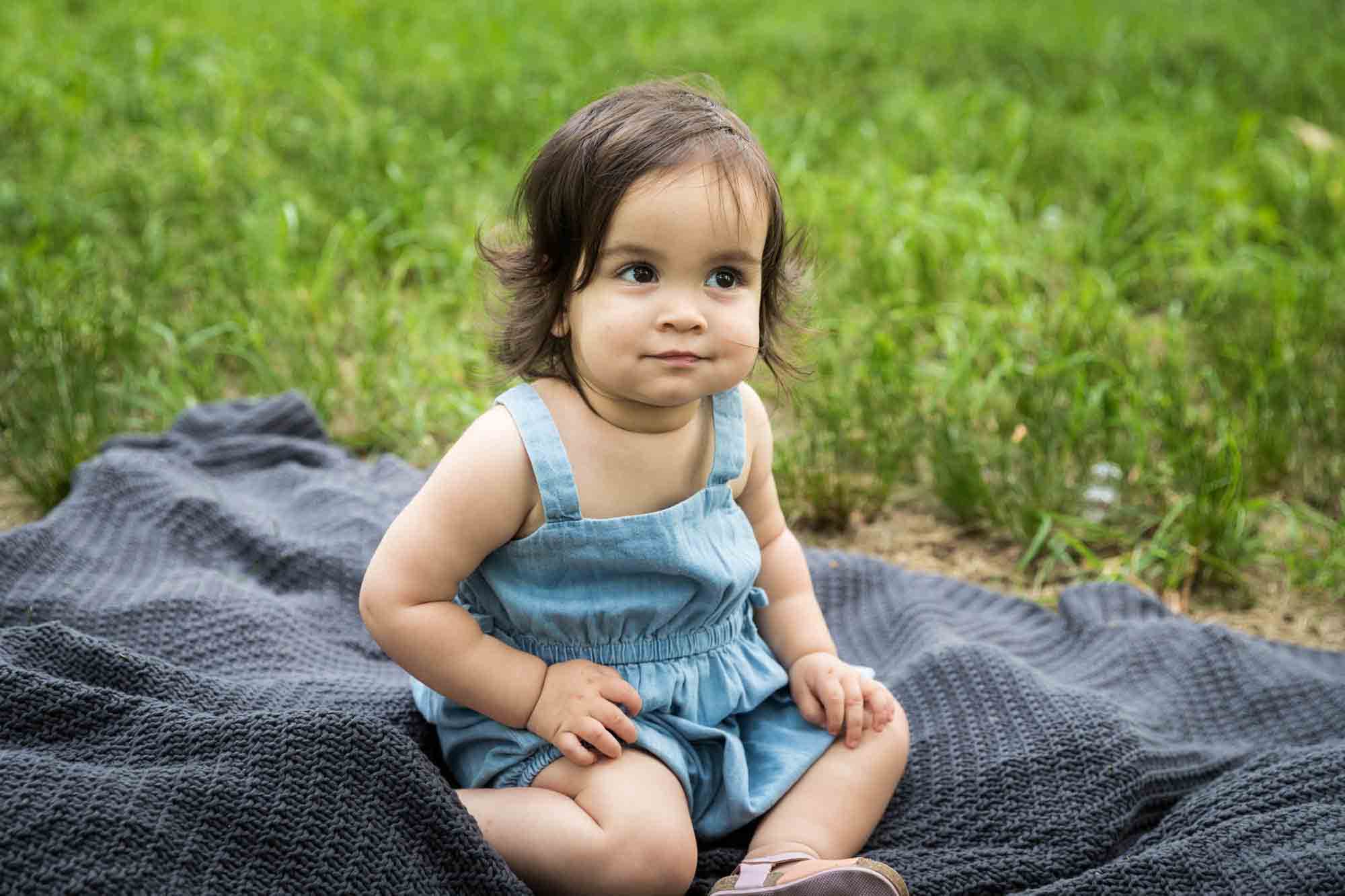 Little girl sitting on a gray blanket in the grass for an article on how to solve family portrait challenges